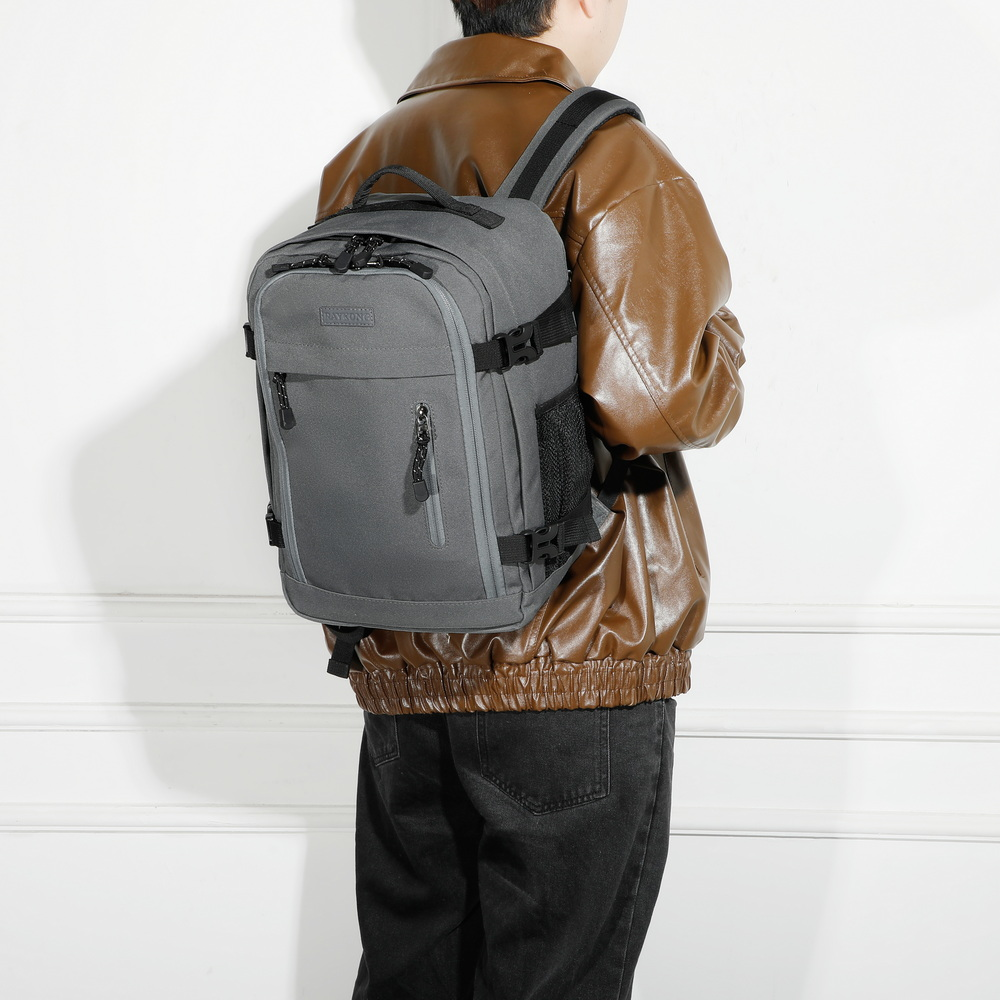 Persona vista desde atrás con una mochila gris, chaqueta de cuero marrón y pantalones oscuros ante pared blanca.