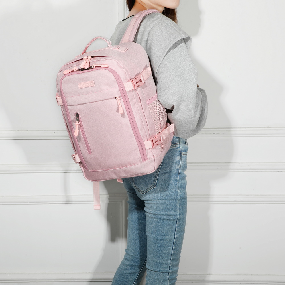 Una mujer con suéter gris y jeans lleva una mochila grande de color rosa claro contra una pared blanca.