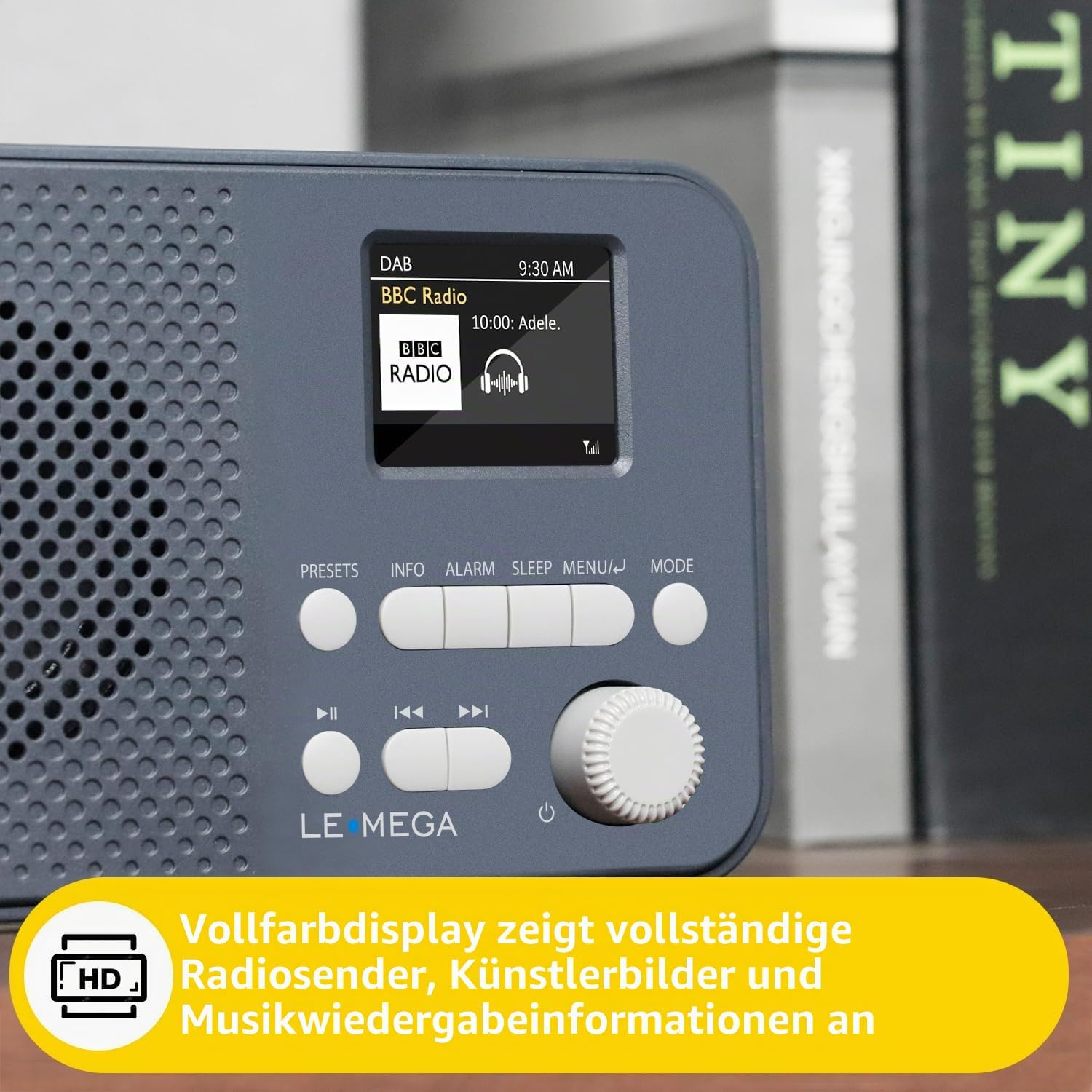 Graues LE MEGA Radio mit Display zeigt BBC Radio, Tasten und Regler davor, Bücher im Hintergrund.