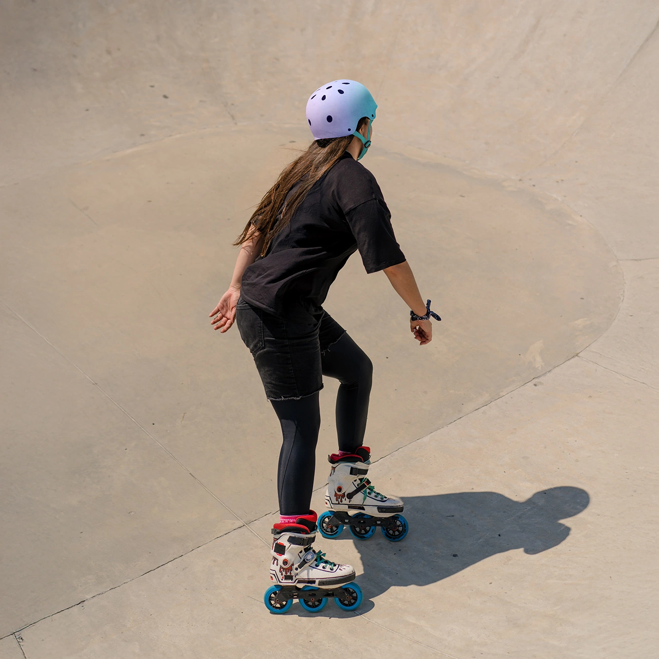 Un pattinatore con casco e abiti neri scivola in una ciotola di cemento per skate.