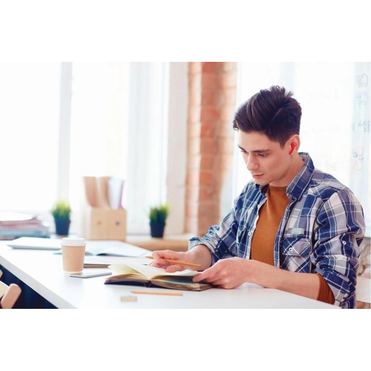 Un joven sentado en un escritorio blanco, leyendo un cuaderno, con una taza de café al lado.