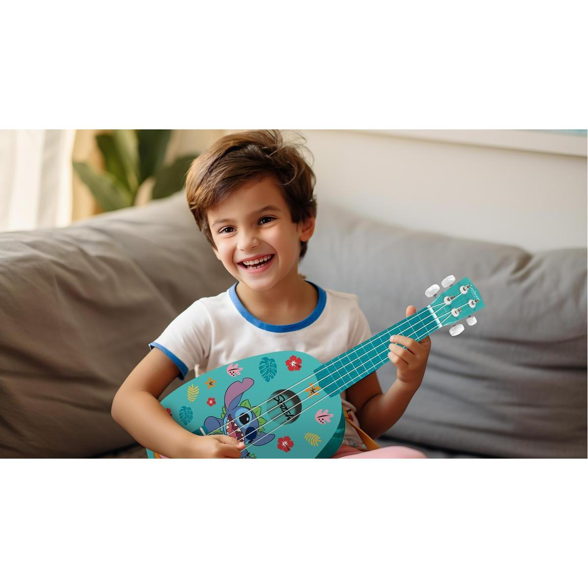 Un niño sonriente está sentado en un sofá gris, tocando un ukelele azul con un diseño de Stitch.