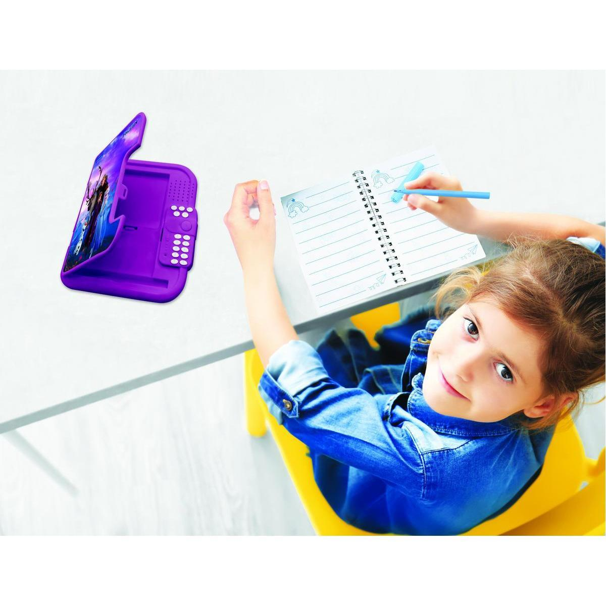 Una niña pequeña con ropa de mezclilla está sentada en una mesa, escribiendo en un cuaderno y sonriendo a la cámara.