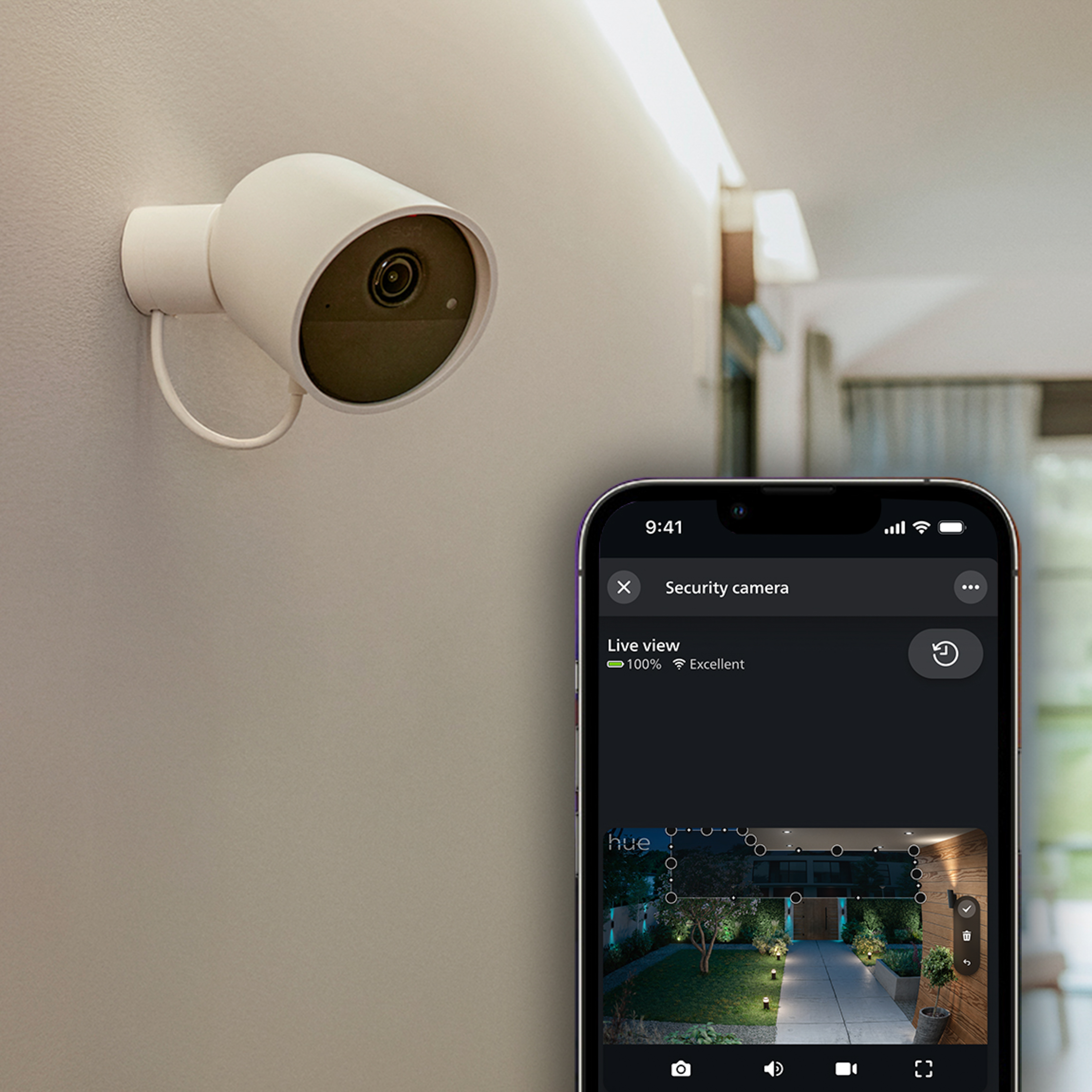 Telecamera di sicurezza bianca su una parete, accanto uno smartphone con la vista in diretta.