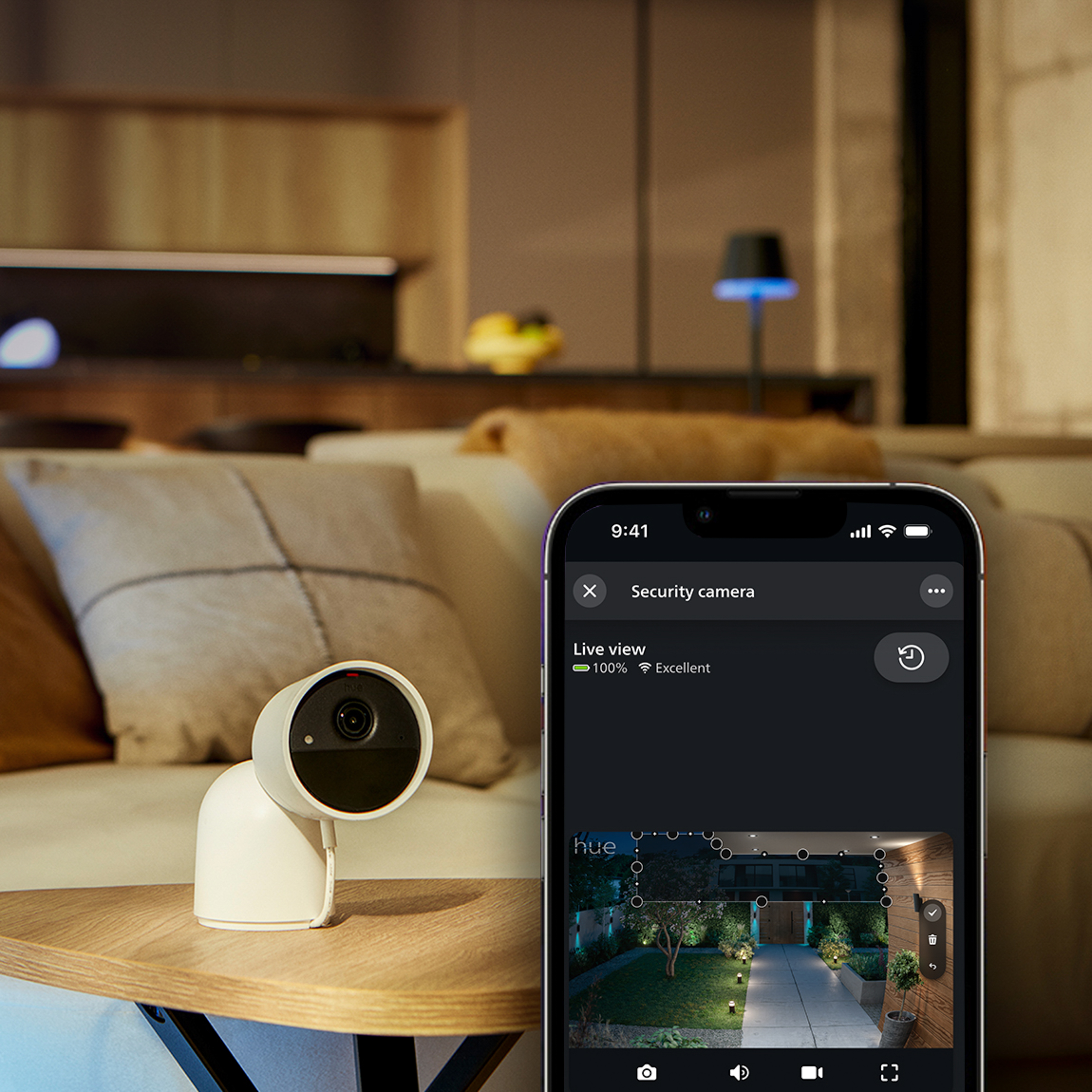 Telecamera di sicurezza bianca su un tavolo; smartphone in primo piano mostra la vista in diretta.