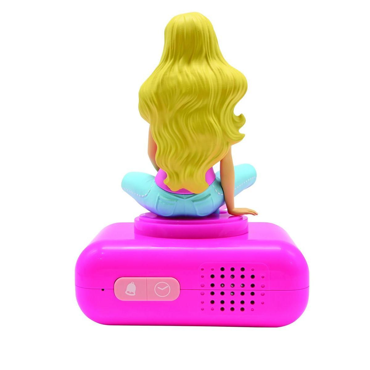 Una figura de Barbie rubia se sienta en una base de despertador rosa brillante sobre fondo blanco.