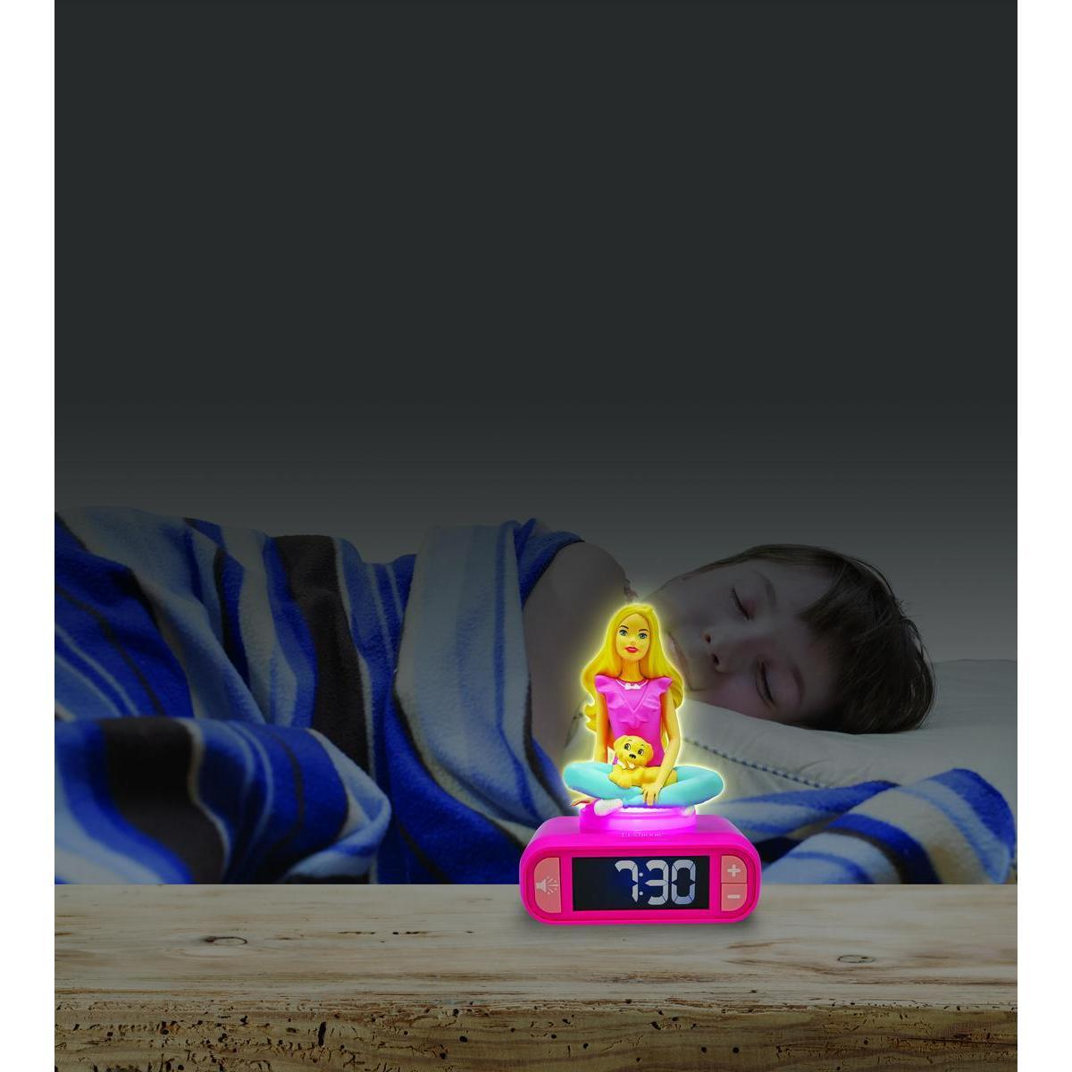 Un despertador rosa brillante de Barbie sobre una mesa de madera; al fondo, un niño duerme con una manta azul.