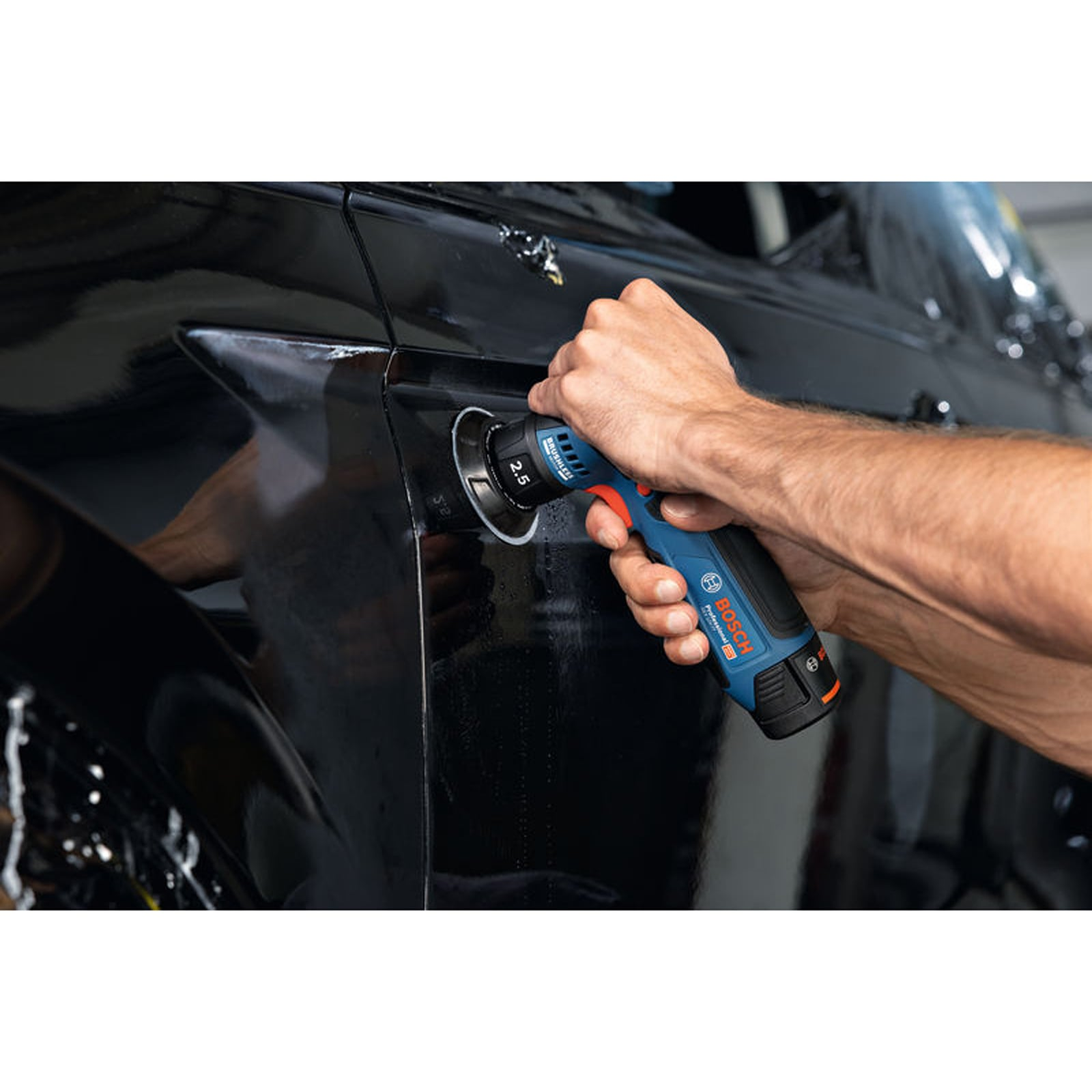 Eine Hände poliert mit einer blauen Bosch Poliermaschine die schwarze Karosserie eines Autos.