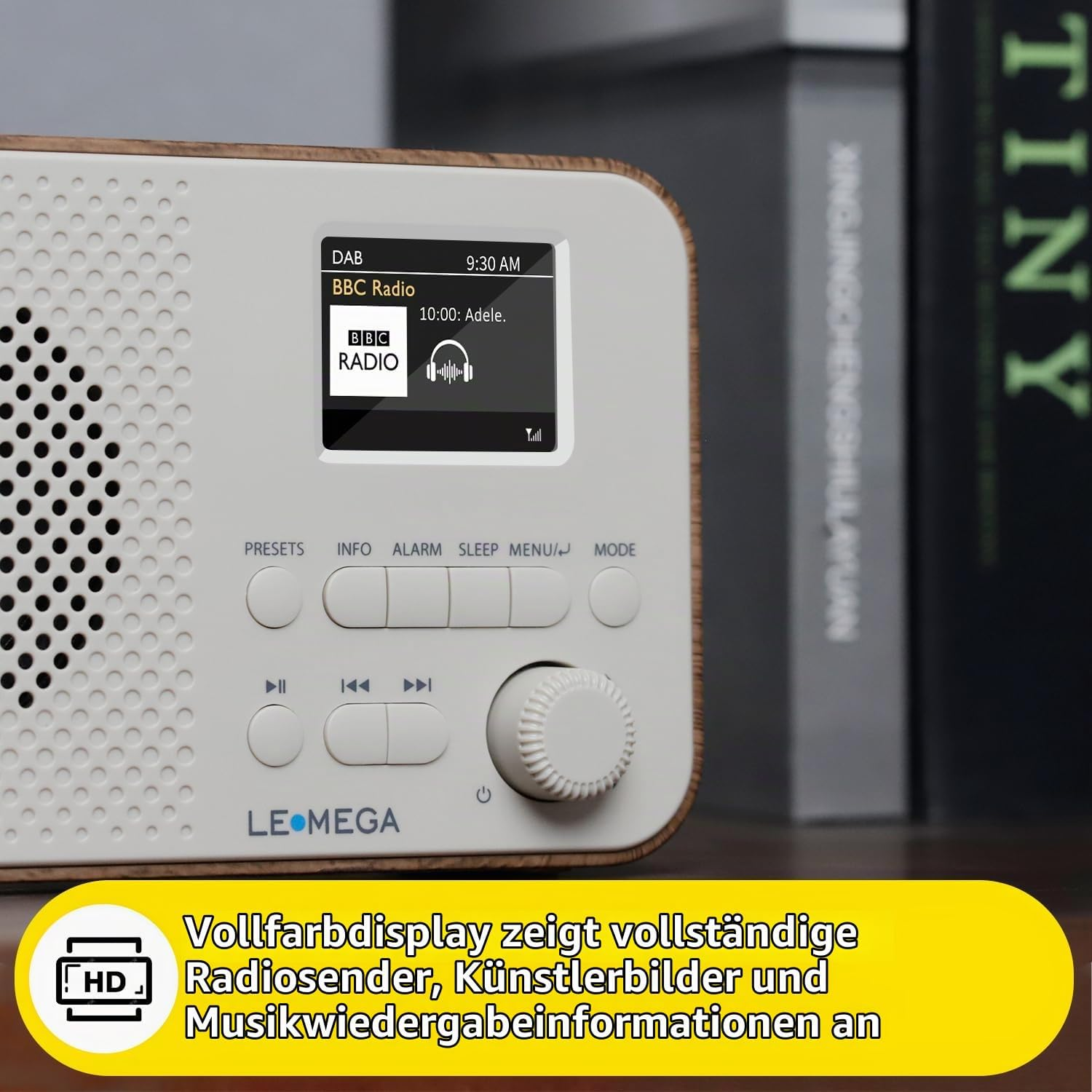 Ein weißes LeMega-Radio mit Holzakzenten, Farbdisplay und Regler auf Holztisch vor Büchern.