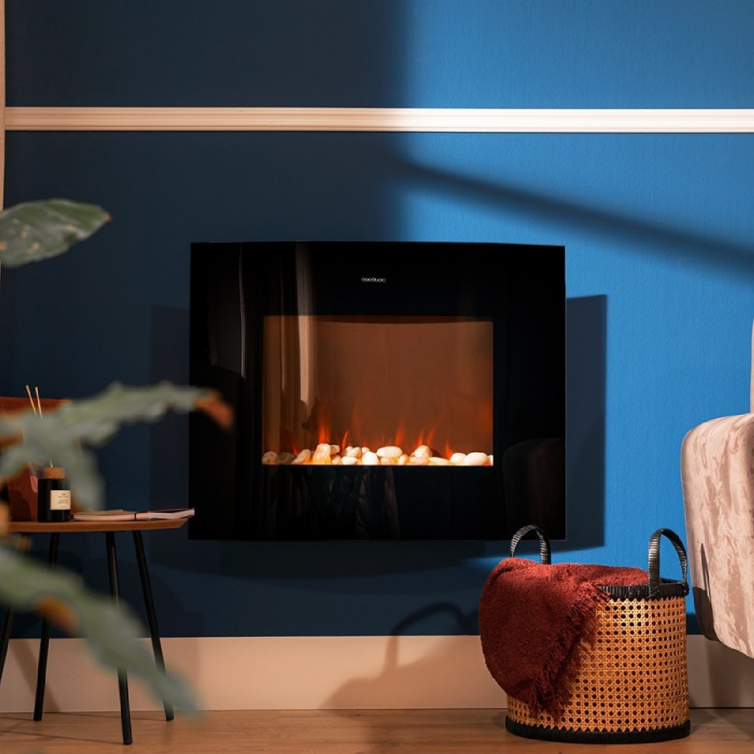 Una chimenea eléctrica cuelga en una pared azul. Abajo a la derecha hay una cesta con una manta roja.