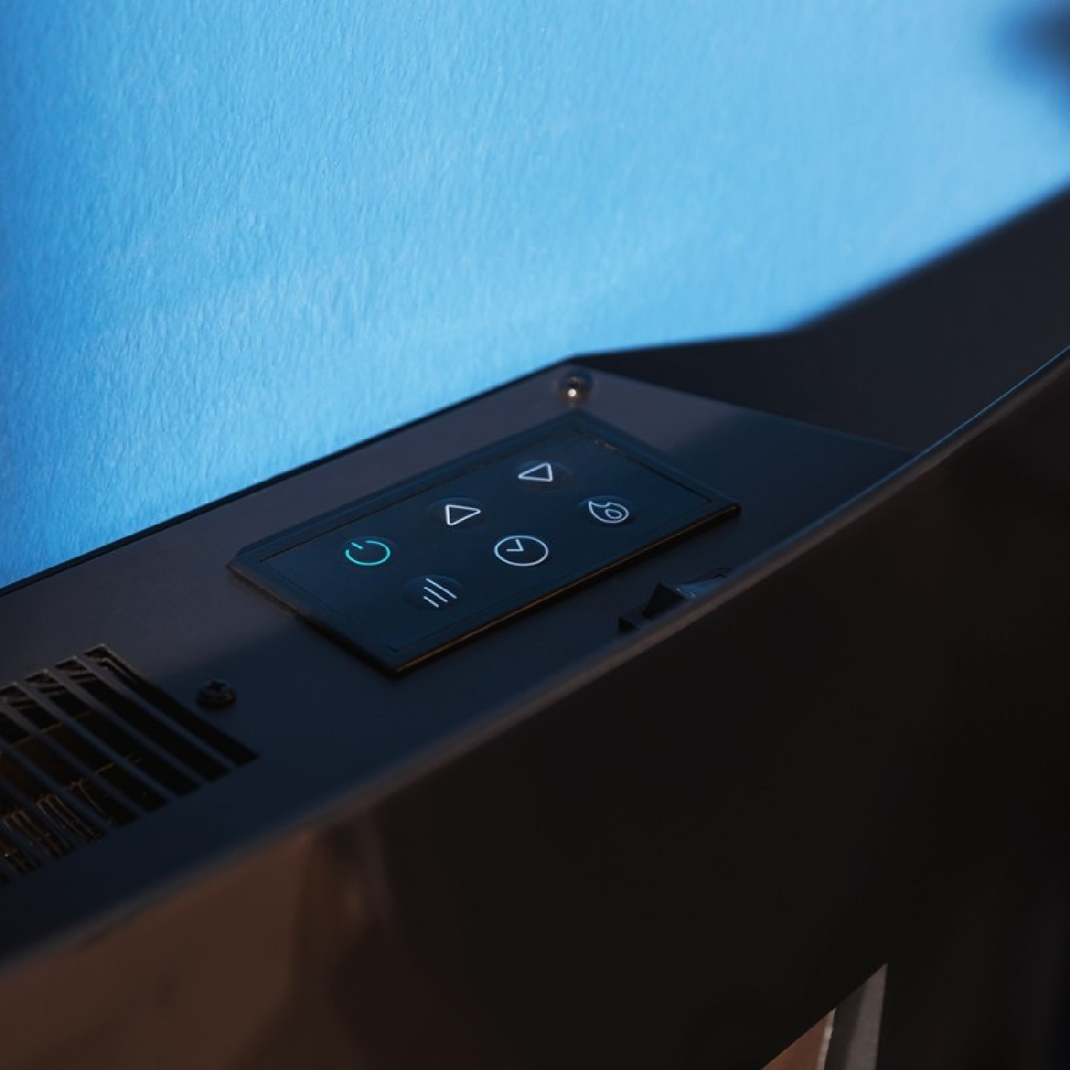 Un panel de control negro con iconos iluminados se encuentra en una superficie oscura frente a una pared azul.