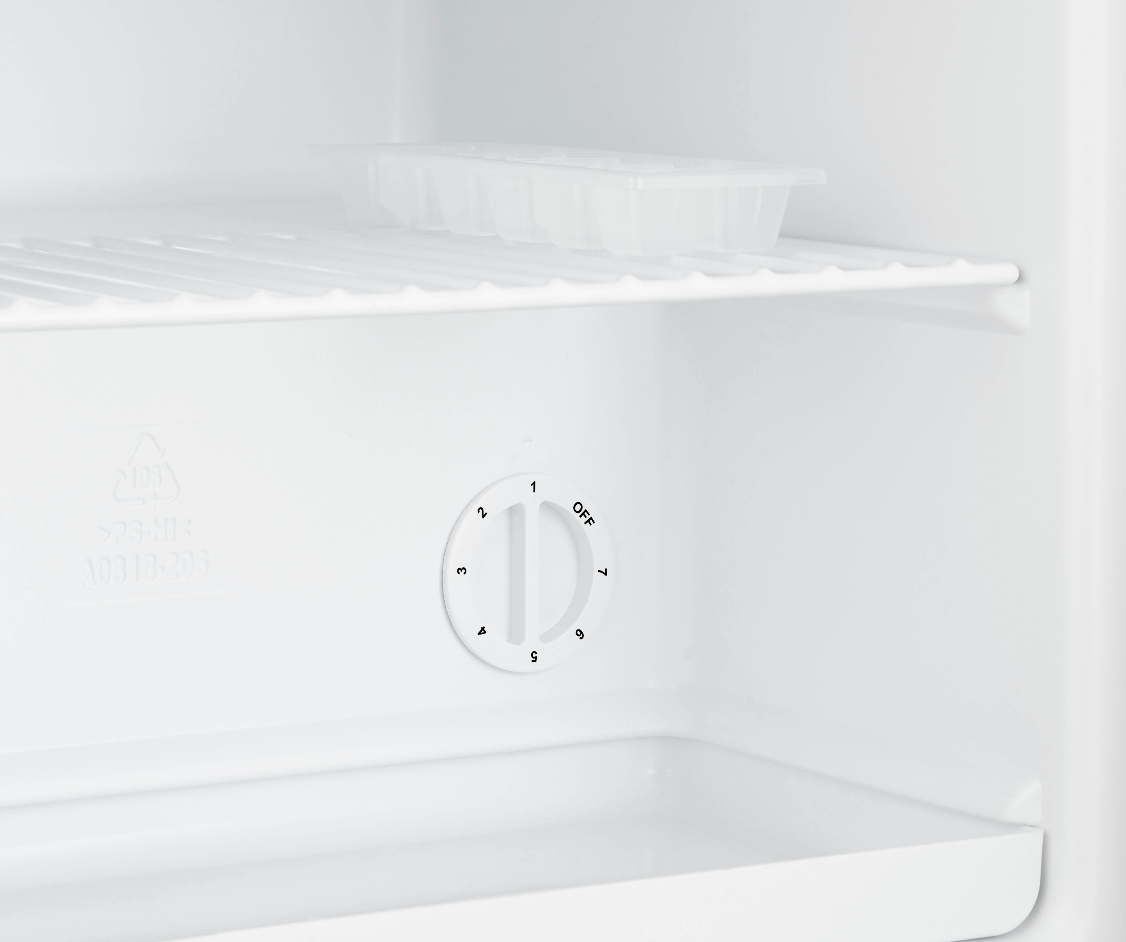 Das Innere eines weißen Kühlschranks mit einem runden Temperaturregler und einer Eisschale im Regal darüber.