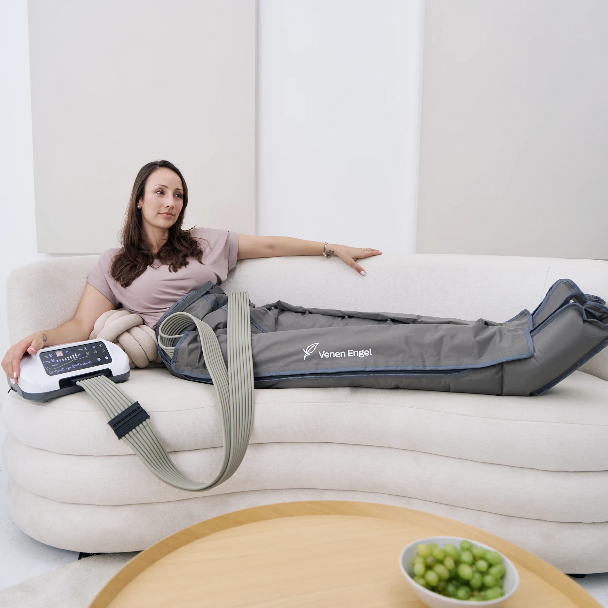 Une femme détendue sur un canapé blanc porte des bottes de compression grises Venen Engel aux jambes.