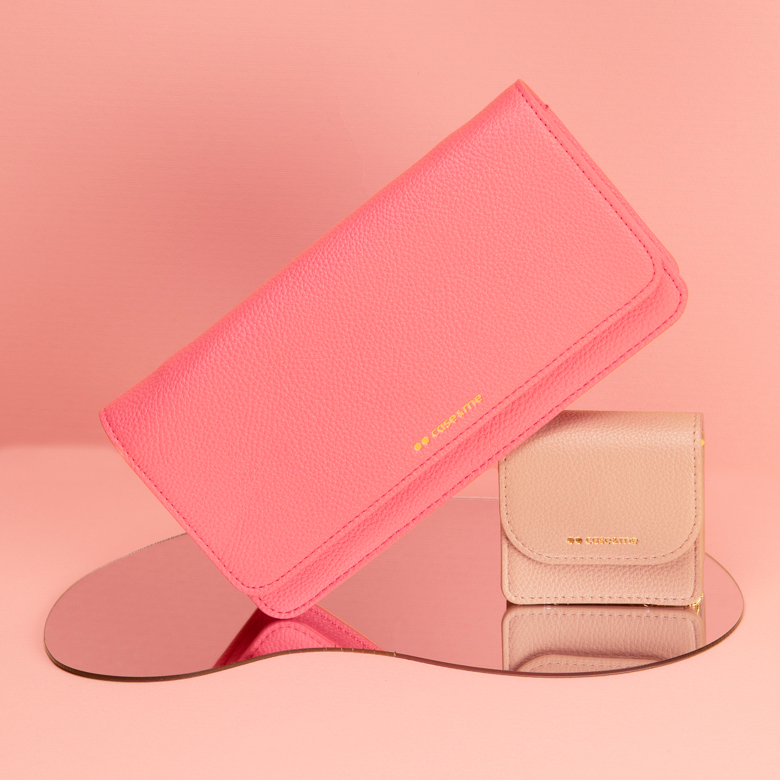 Un bolso rosa y una cartera beige están sobre un espejo contra un fondo rosa.