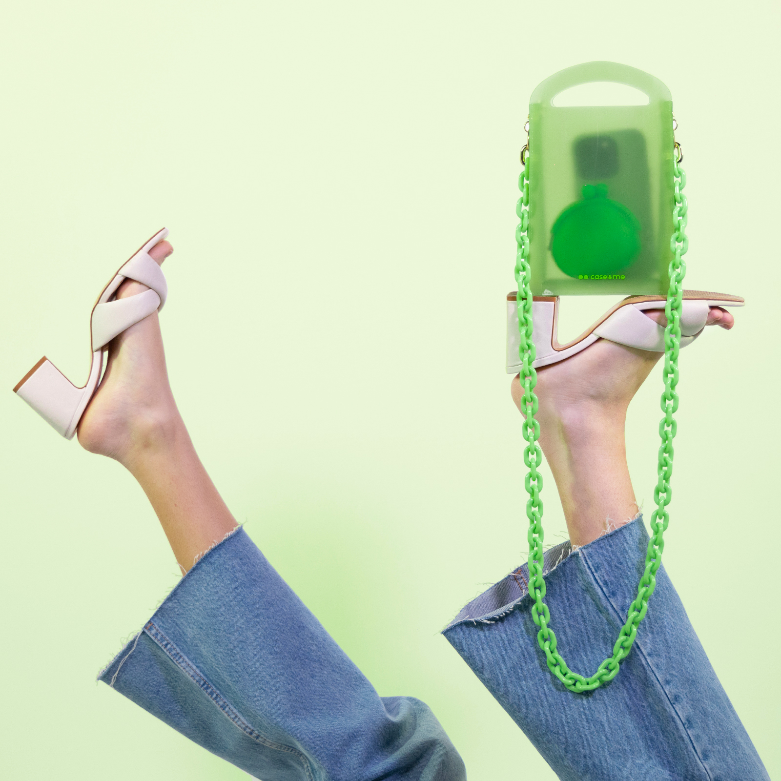 Piernas en jeans y tacones en el aire, el pie derecho sostiene un bolso verde.