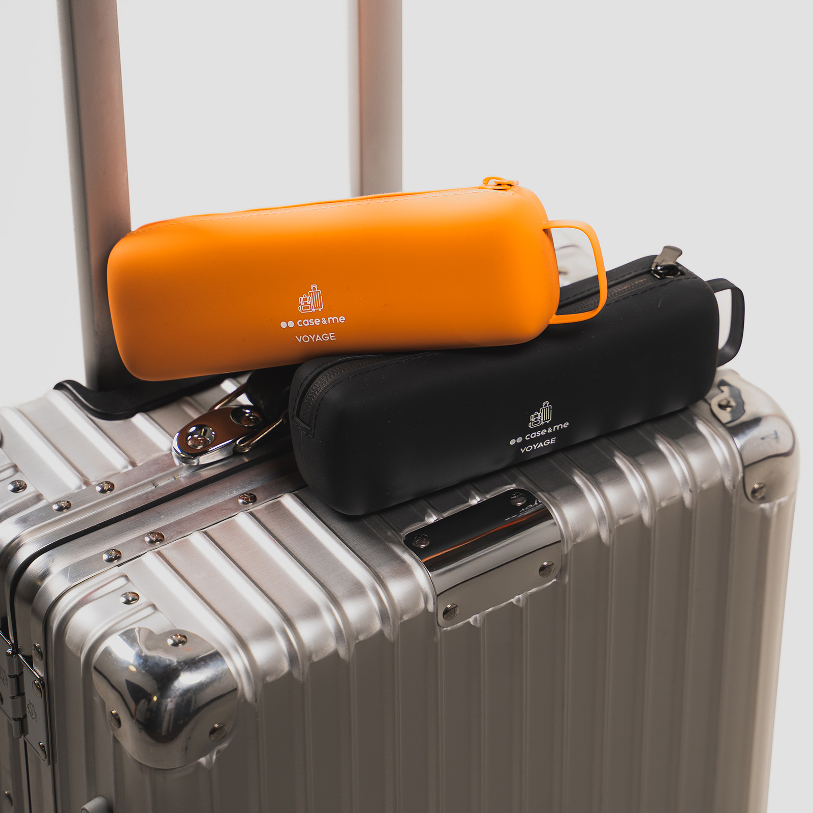 Un estuche naranja y otro negro encima de una maleta metálica plateada.