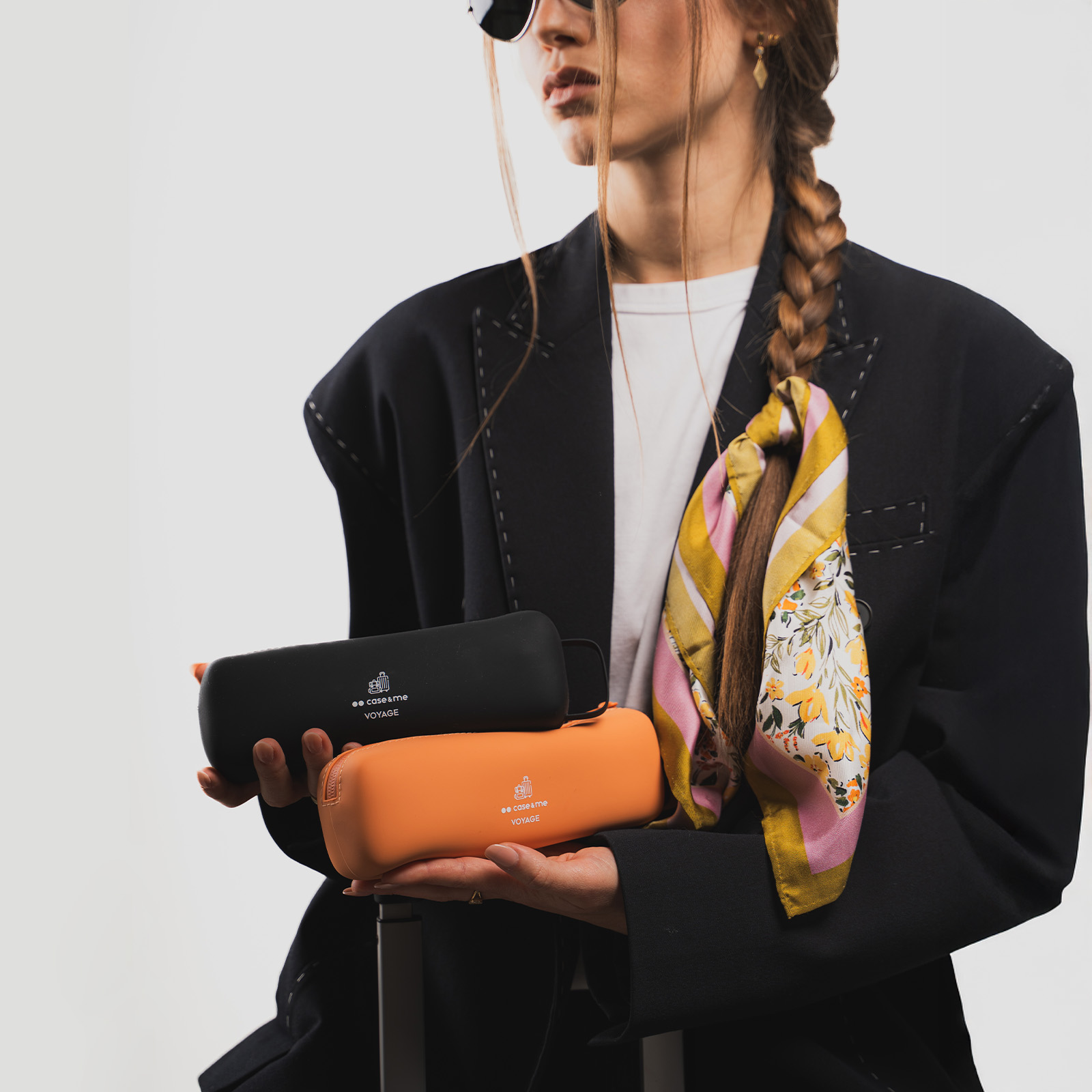 Una mujer con chaqueta negra y pañuelo sostiene estuches de gafas negros y naranjas.