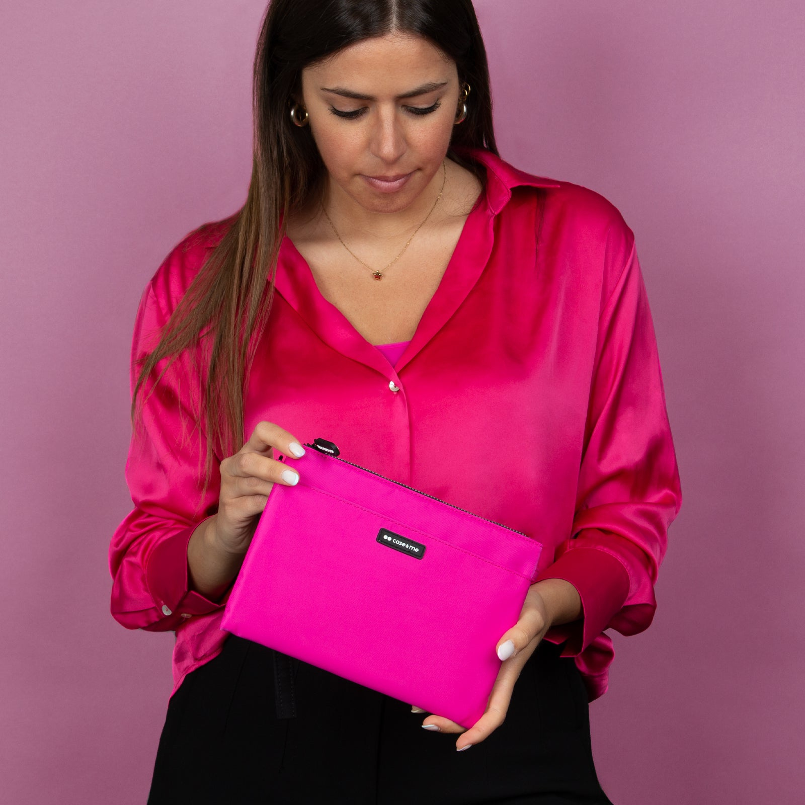 Una mujer con una camisa rosa sostiene un estuche rosa a juego sobre un fondo rosa.