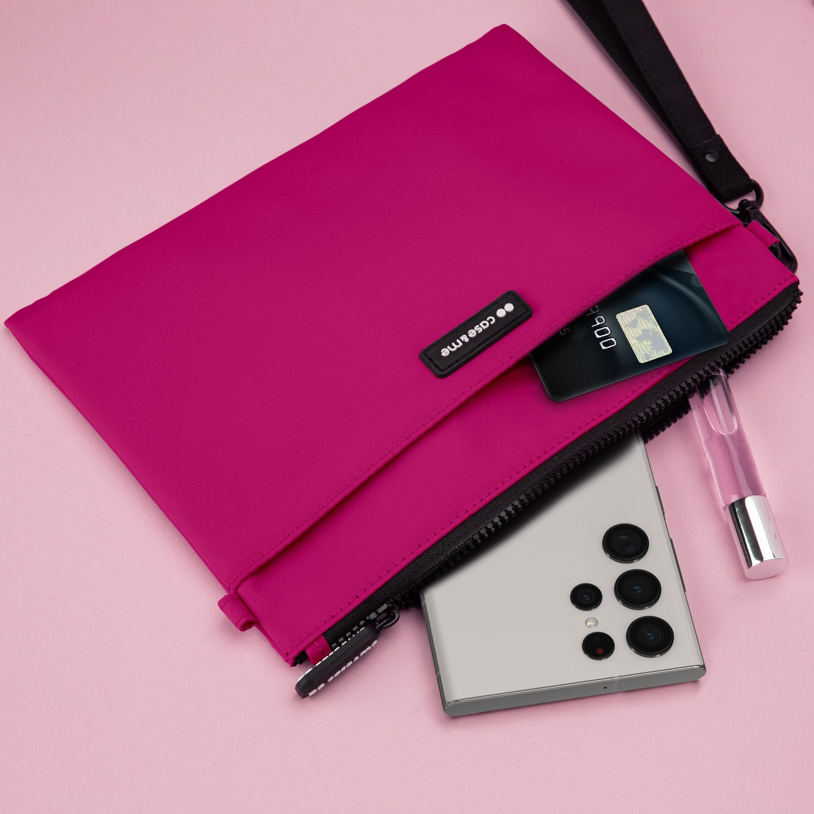 Un estuche rosa con cremallera, un móvil, una tarjeta y un frasco de perfume sobre fondo rosa.