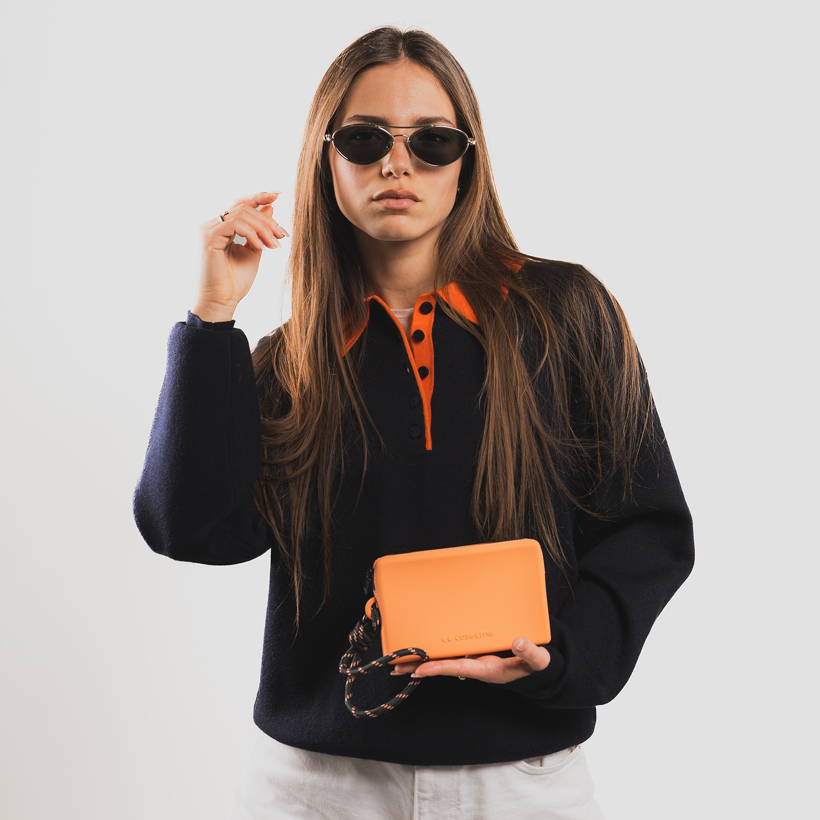 Una mujer con gafas de sol y un suéter negro sostiene un bolso pequeño de color naranja.