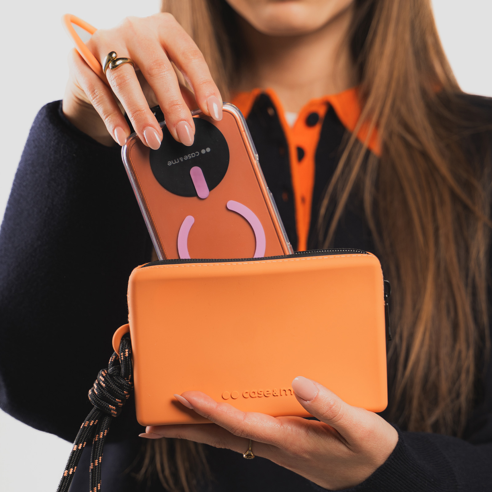 Una persona coloca un teléfono naranja en una bolsa de silicona naranja con correa de cordón negro.