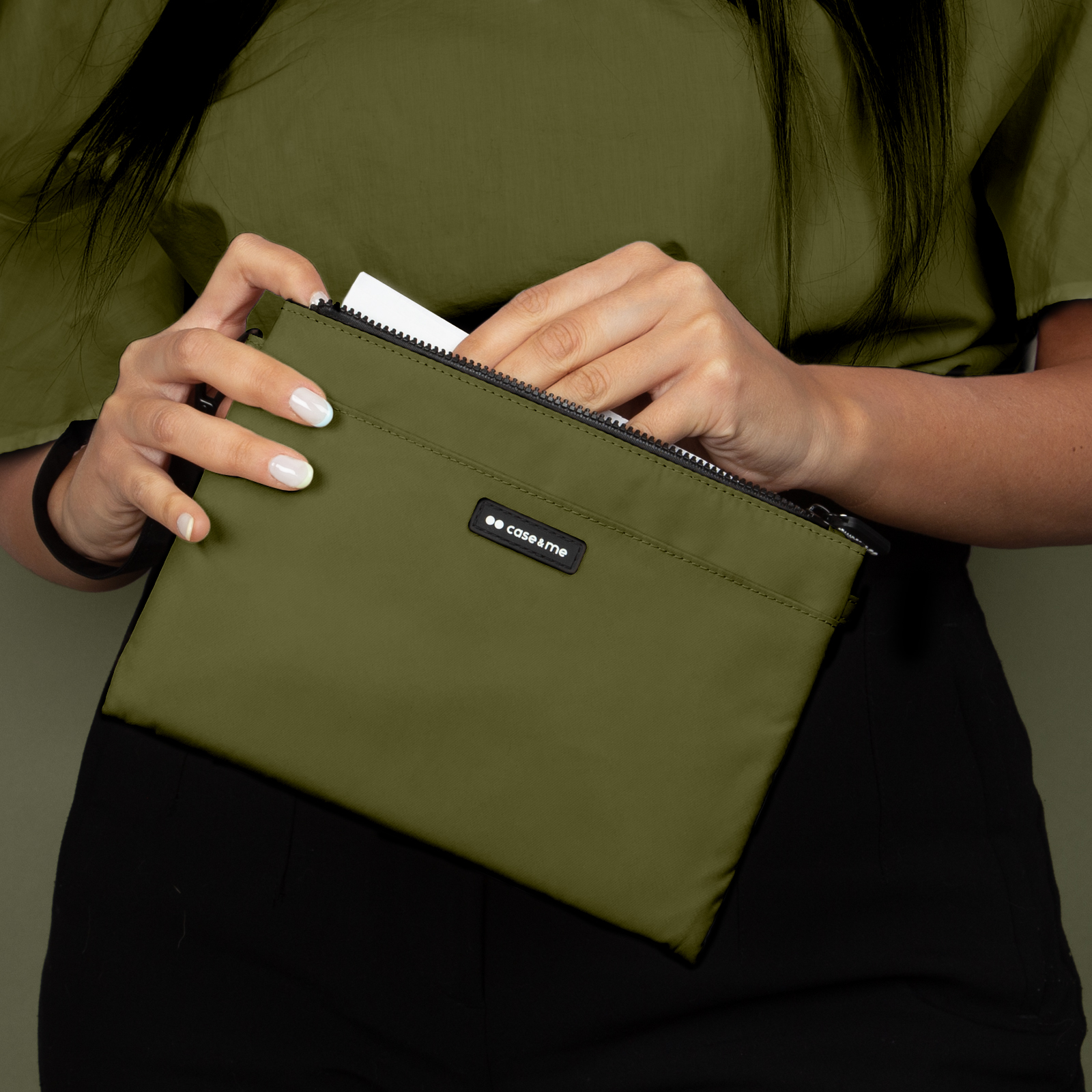 Una persona con camisa verde oliva abre un estuche verde oliva a juego con cremallera.