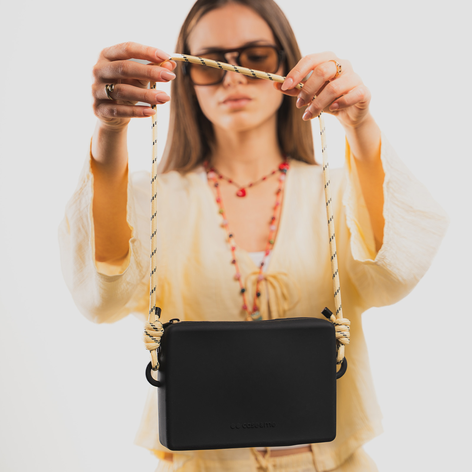 Una mujer con ropa amarilla y gafas de sol sostiene un bolso negro cruzado con correa de cuerda.