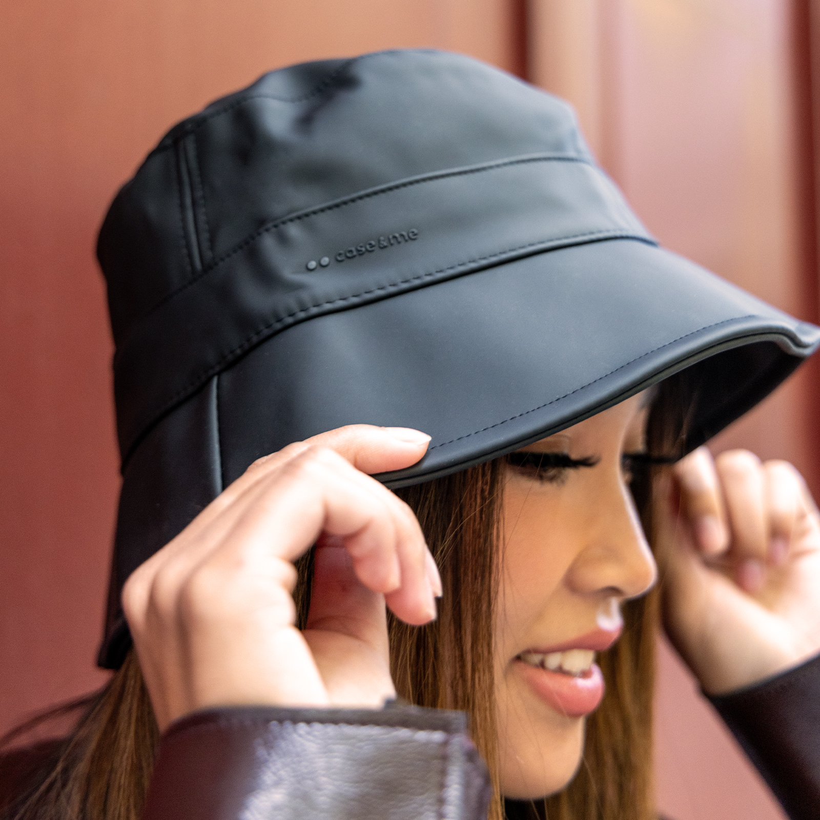 Una mujer con un sombrero de pescador negro con el texto case and me, ajustándose el ala.