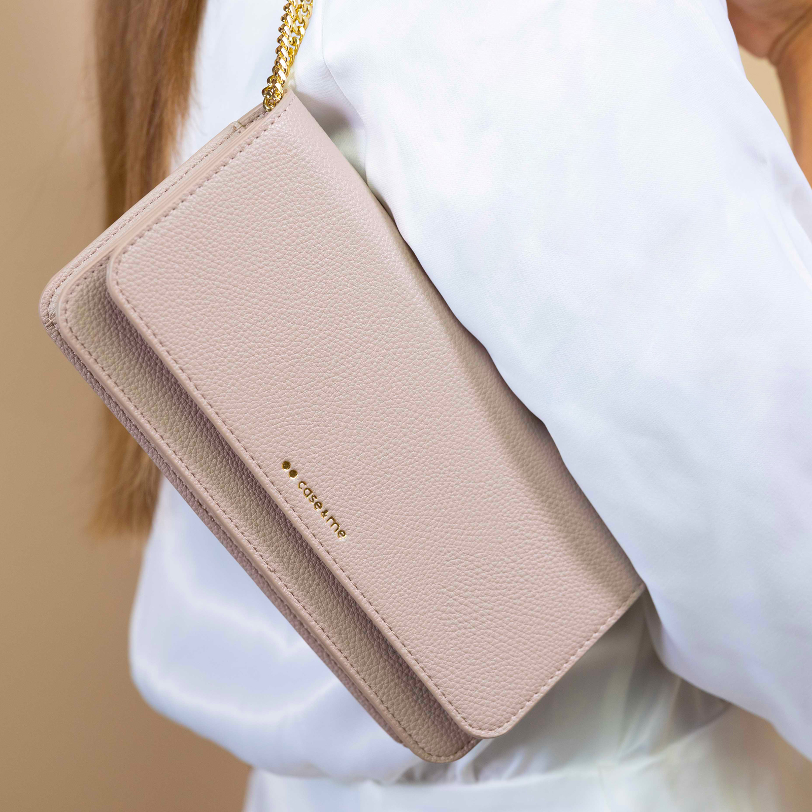 Un bolso cruzado beige con cadena dorada llevado por una mujer con blusa blanca.