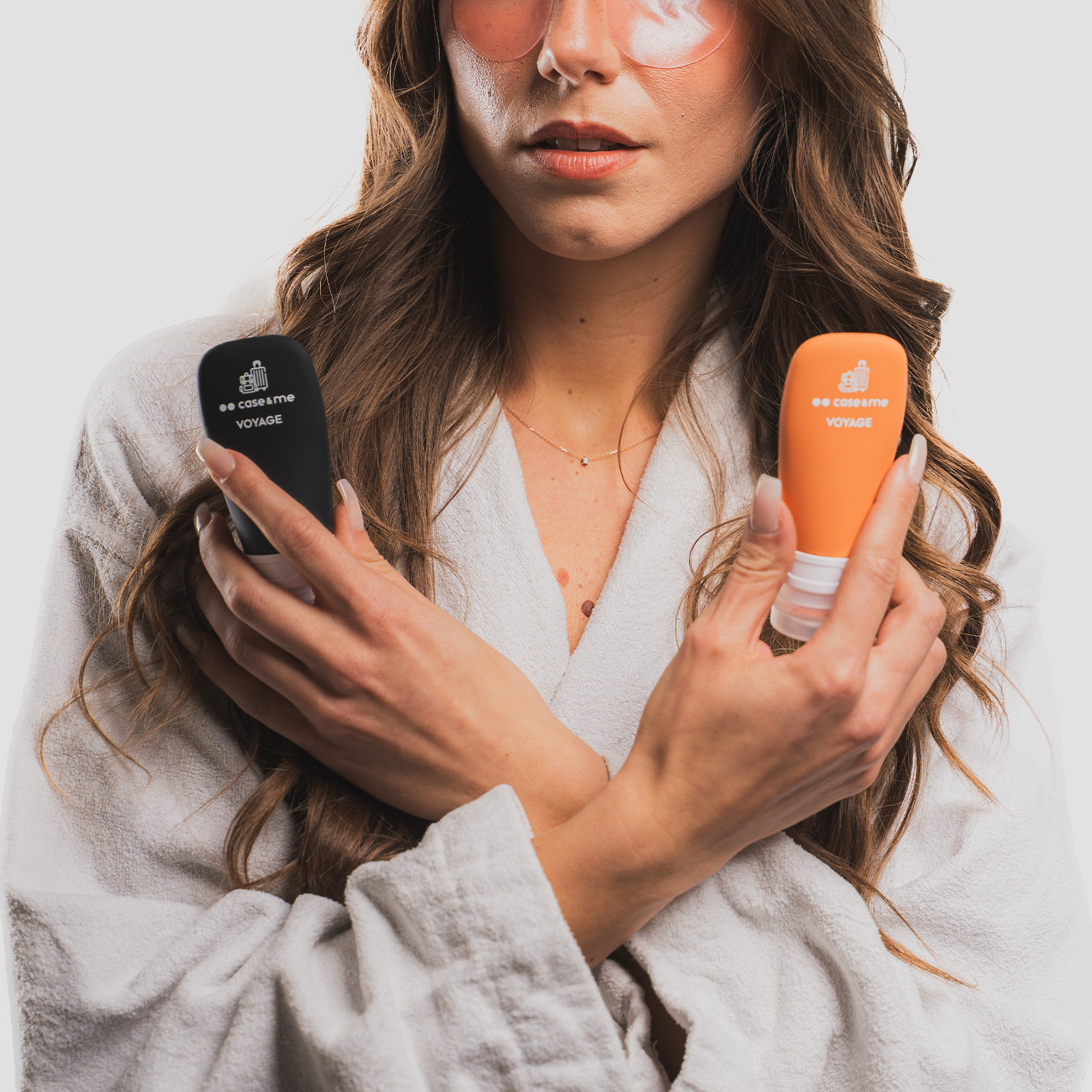 Una mujer en bata blanca sostiene dos pequeñas botellas de cosméticos, una negra y otra naranja, contra su pecho.
