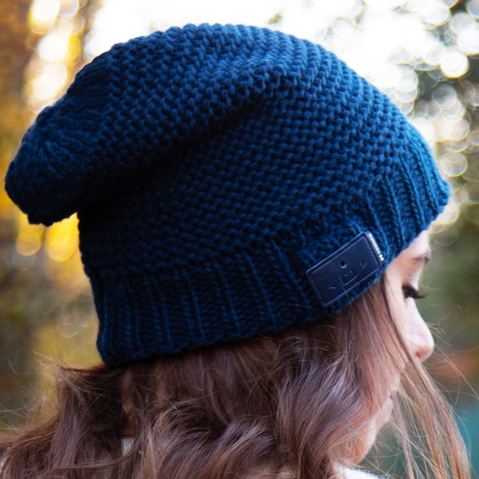 Una donna con berretto in maglia blu scuro e capelli castani all'aperto con sfondo sfocato.
