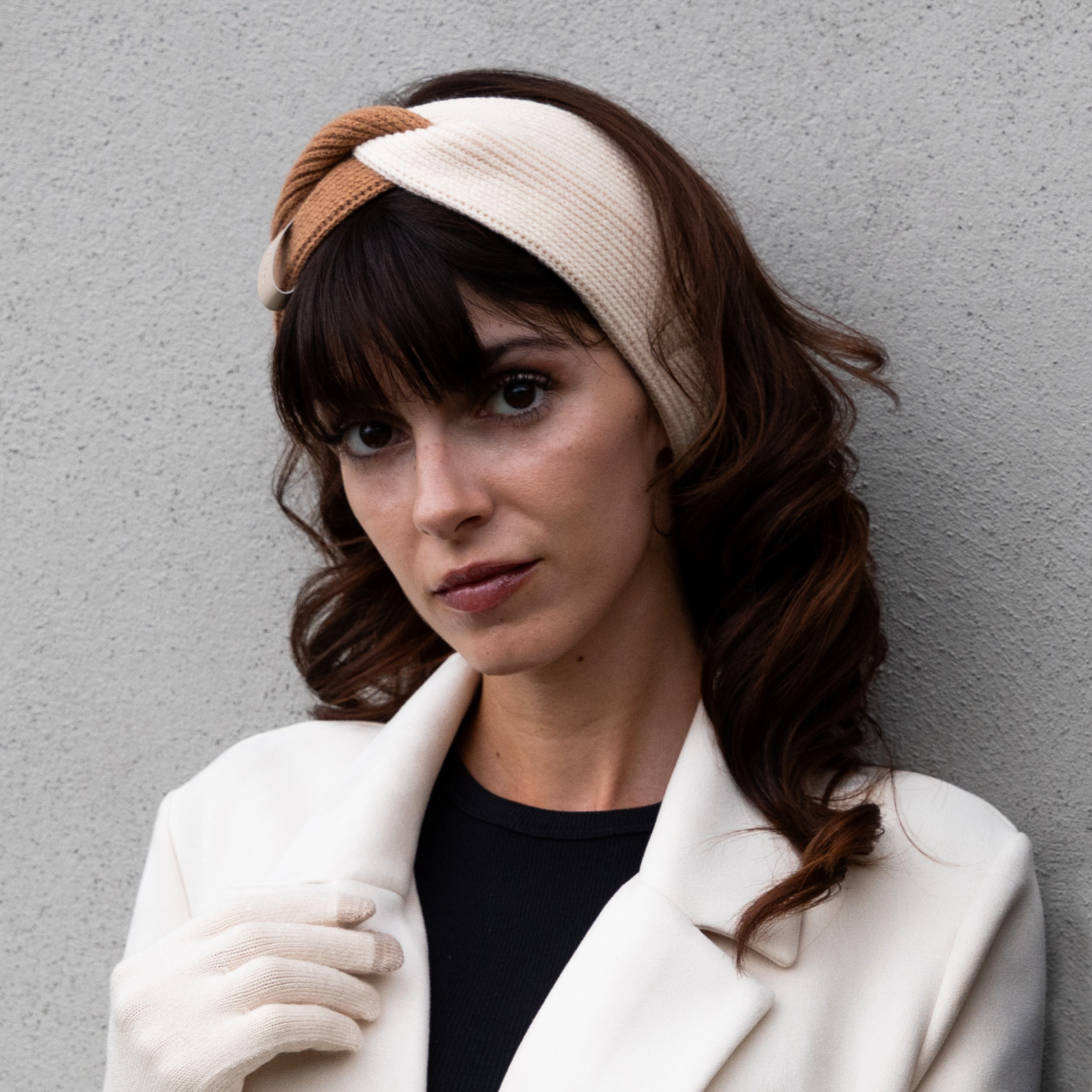 Una donna con i capelli scuri indossa una fascia bianca e marrone, cappotto bianco e guanti abbinati.