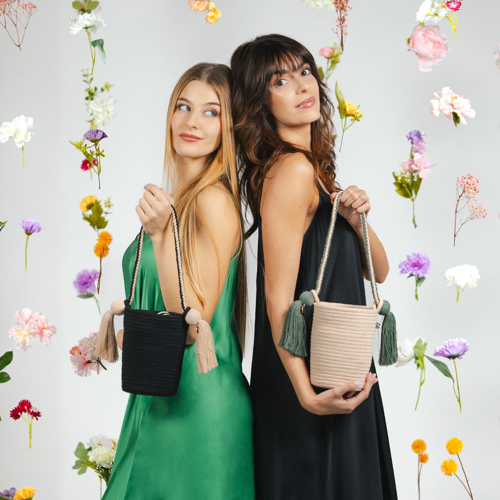 Dos mujeres con vestidos sostienen bolsos hechos a mano sobre un fondo de flores flotantes.