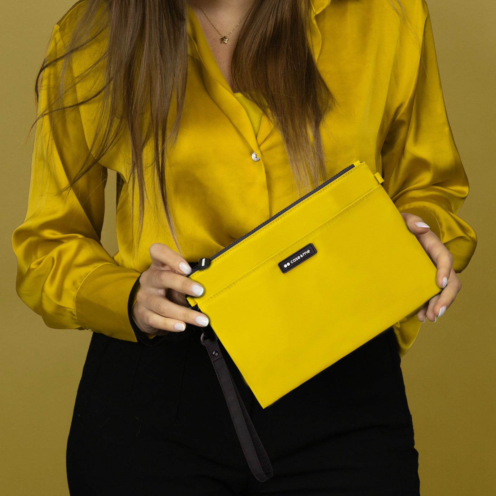 Una mujer con camisa amarilla sostiene un bolso de mano amarillo con cremallera negra.