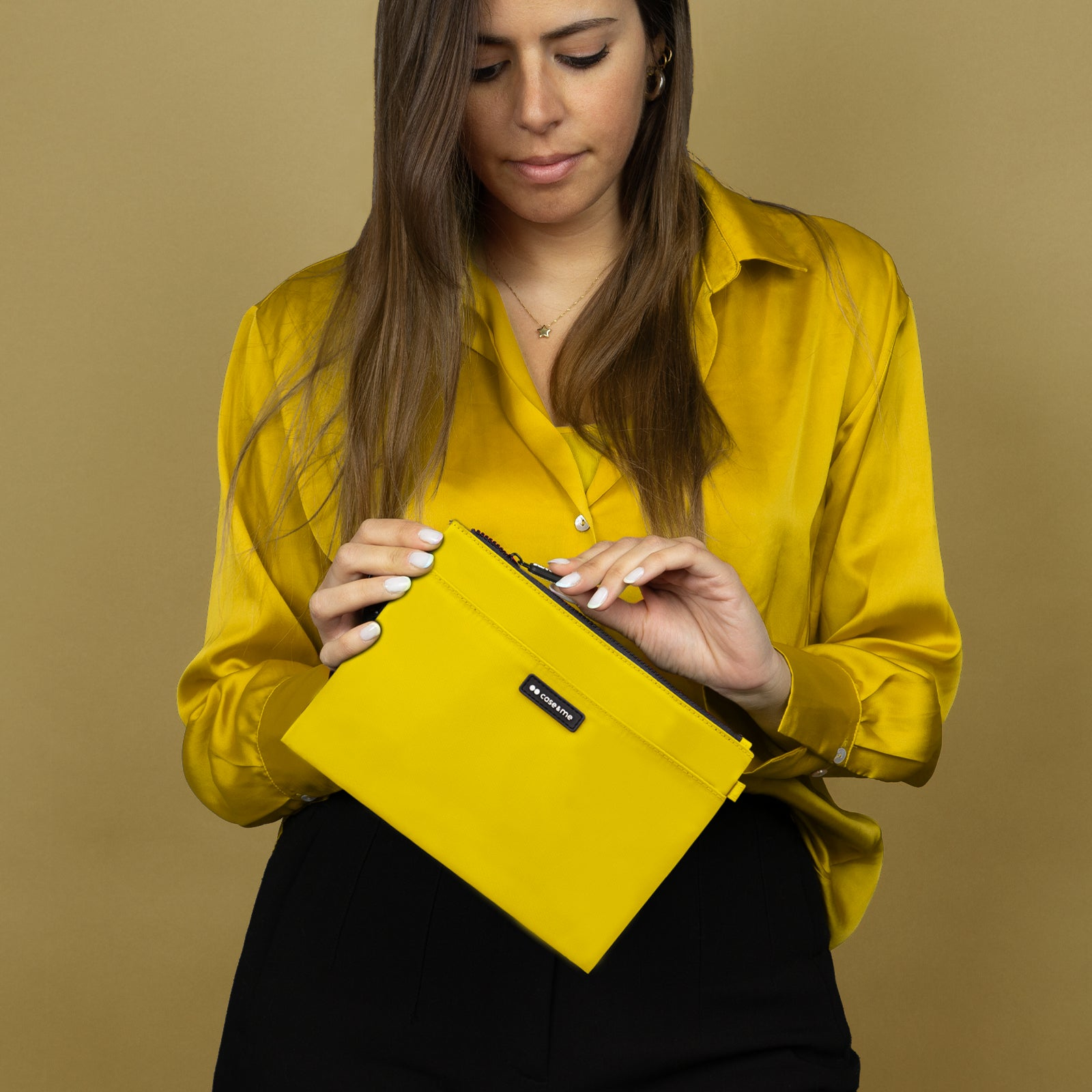 Una mujer con blusa amarilla y pantalones negros abre un pequeño estuche amarillo con cremallera.