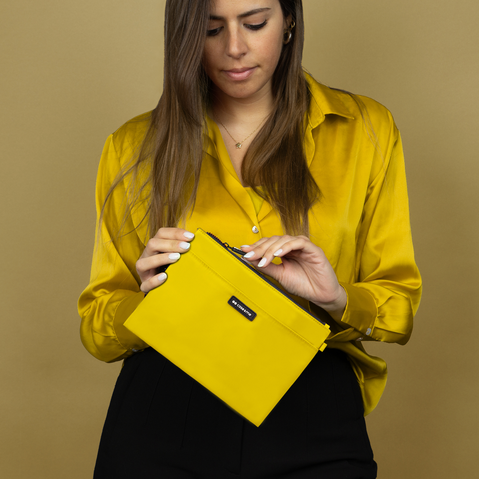Una mujer con camisa amarilla y pantalones negros sostiene y abre un estuche amarillo.