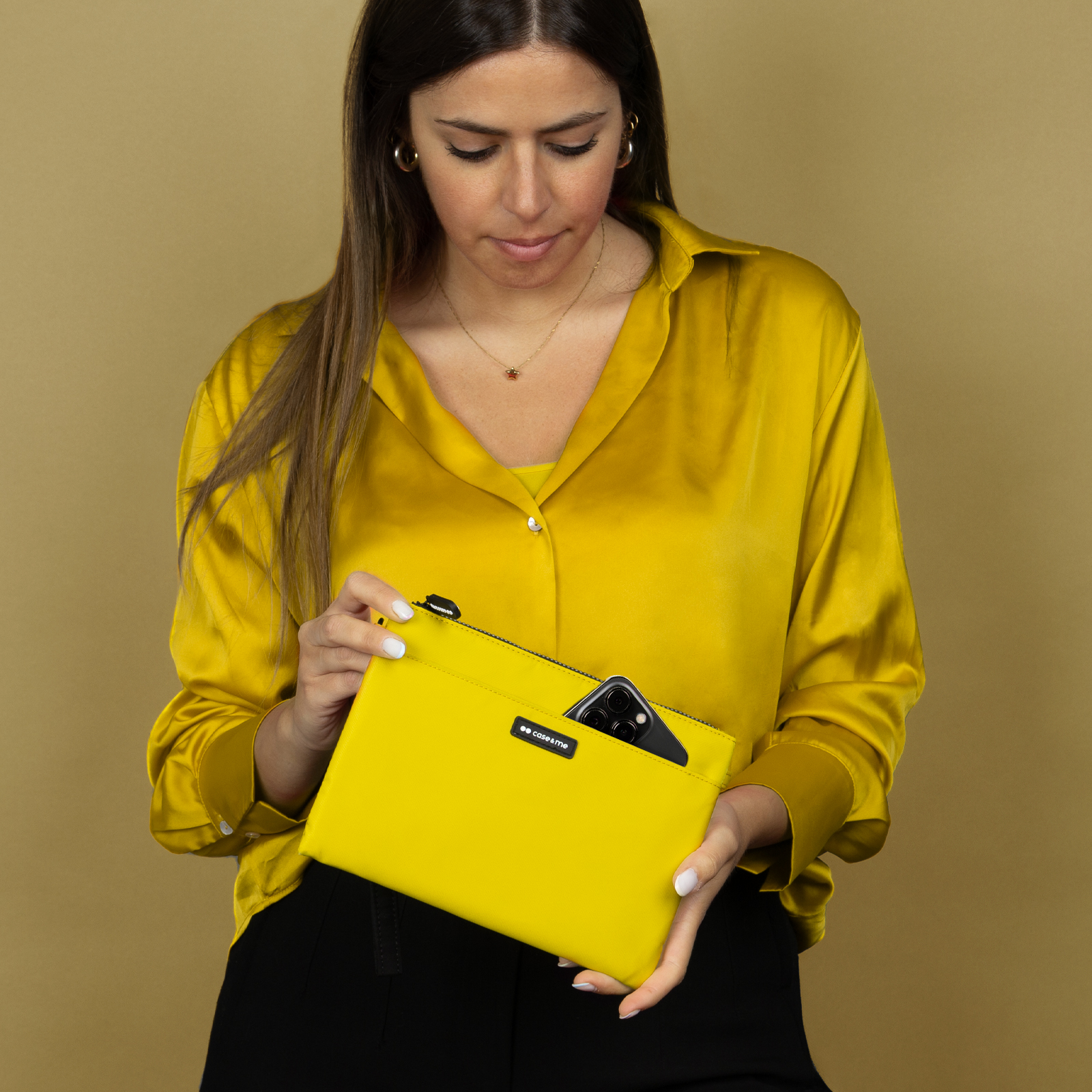 Una mujer con blusa amarilla sostiene un bolso amarillo con un smartphone dentro sobre fondo beige.