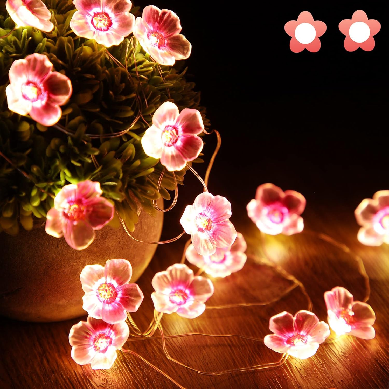 Rosa LED-Blumenlichterkette leuchtet im Dunkeln um ein Grün.