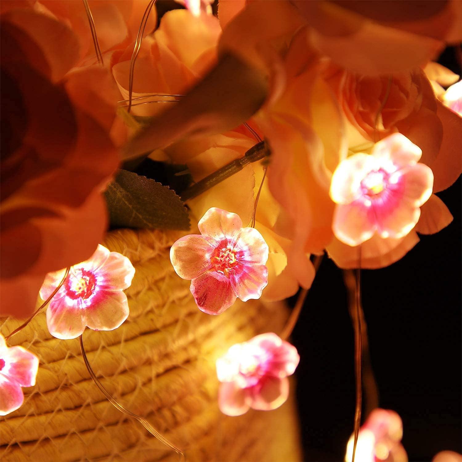 Leuchtende rosa Lichterketten in Blütenform, verflochten mit Kunstrosen.
