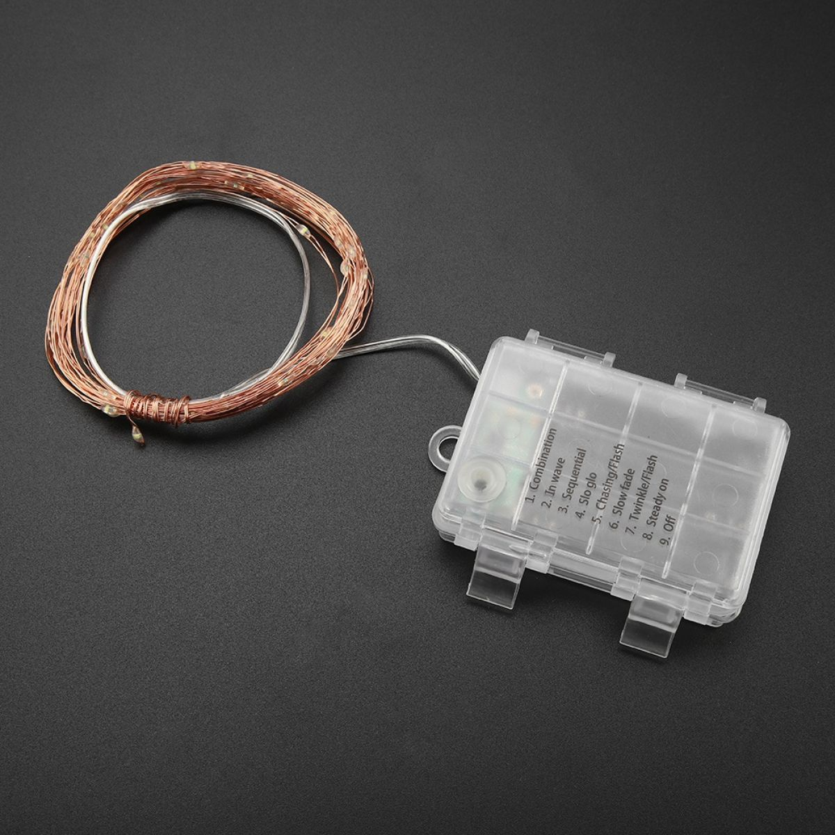 Eine Spule Kupfer-Lichterkette verbunden mit einer transparenten Batteriebox auf dunklem Hintergrund.