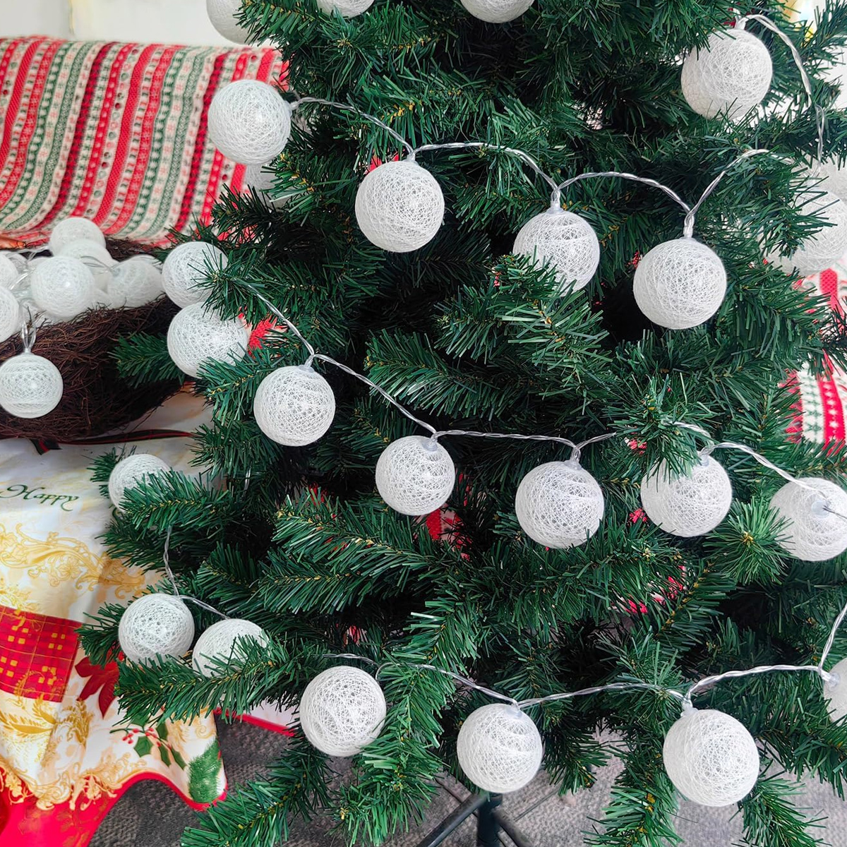 Ein grüner Weihnachtsbaum ist mit einer Lichterkette aus weißen Stoffkugeln geschmückt.