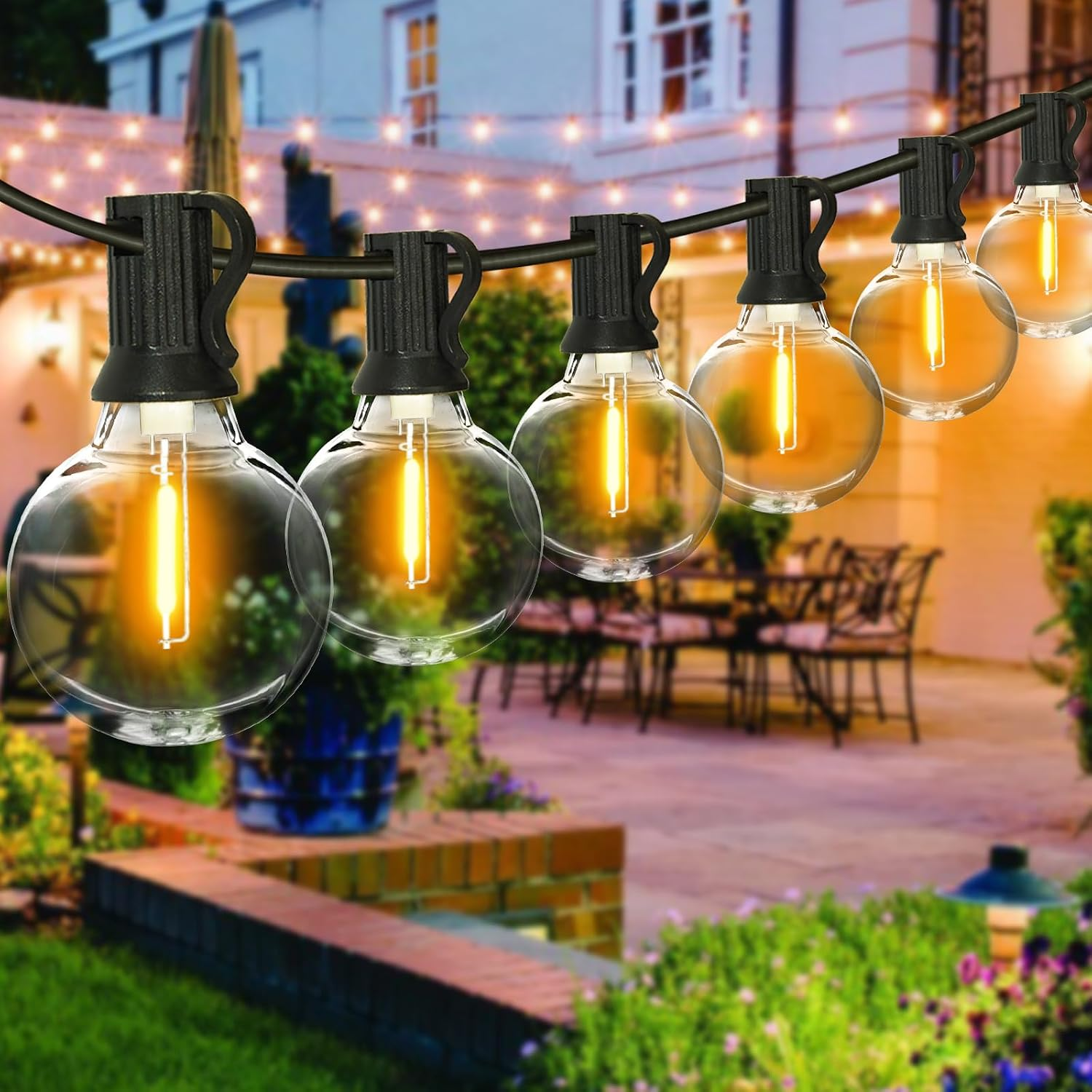 Lichterkette mit runden Glühbirnen im Vordergrund, beleuchteter Garten im Hintergrund.