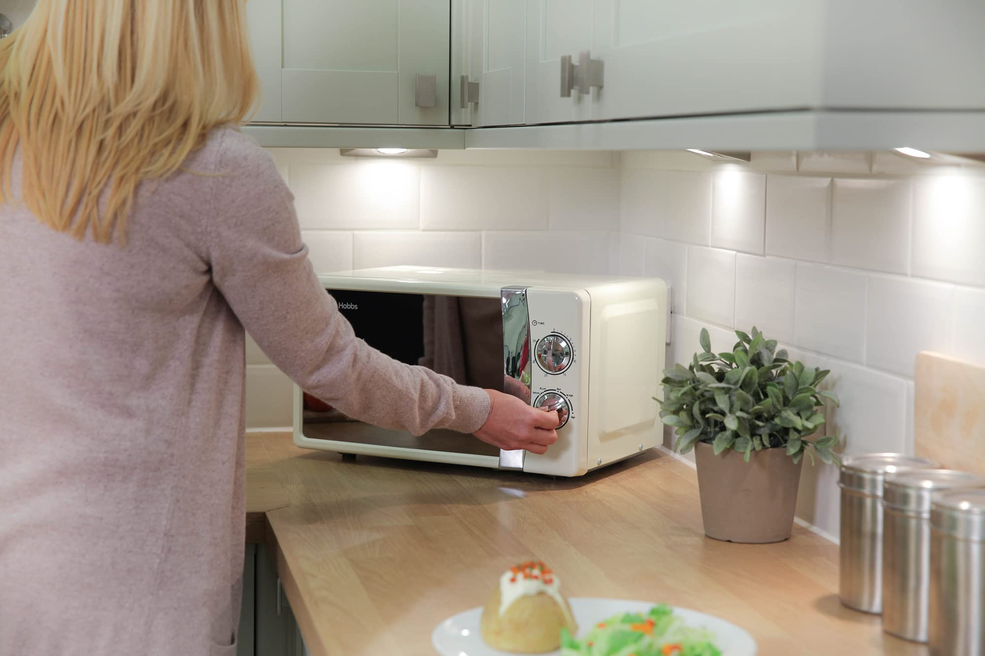 Una donna bionda aziona un forno a microonde crema in cucina.