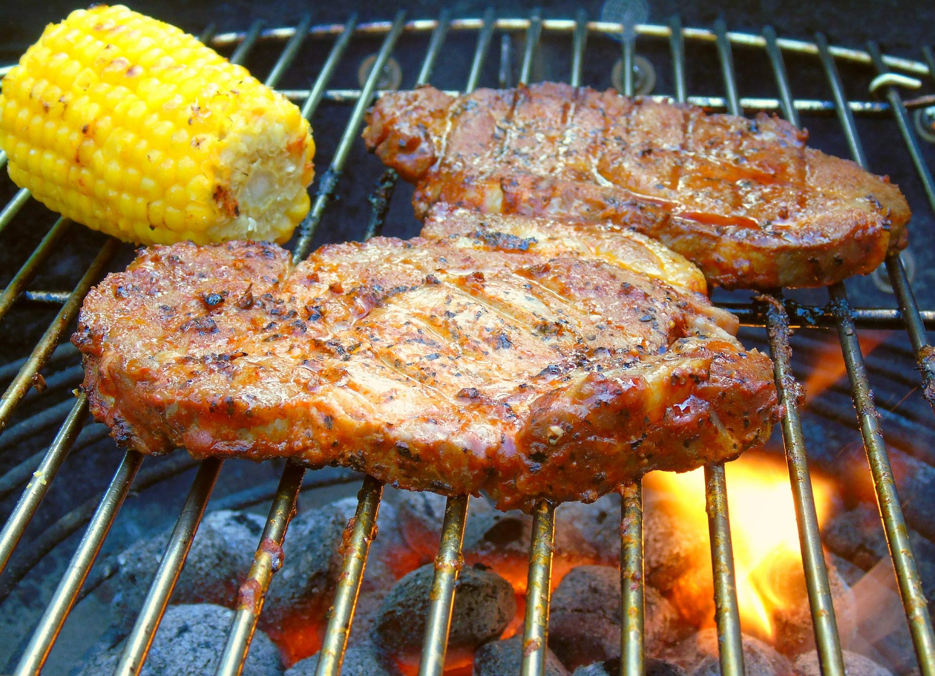 Deux steaks grillés et un épi de maïs sur un gril au-dessus de charbons.