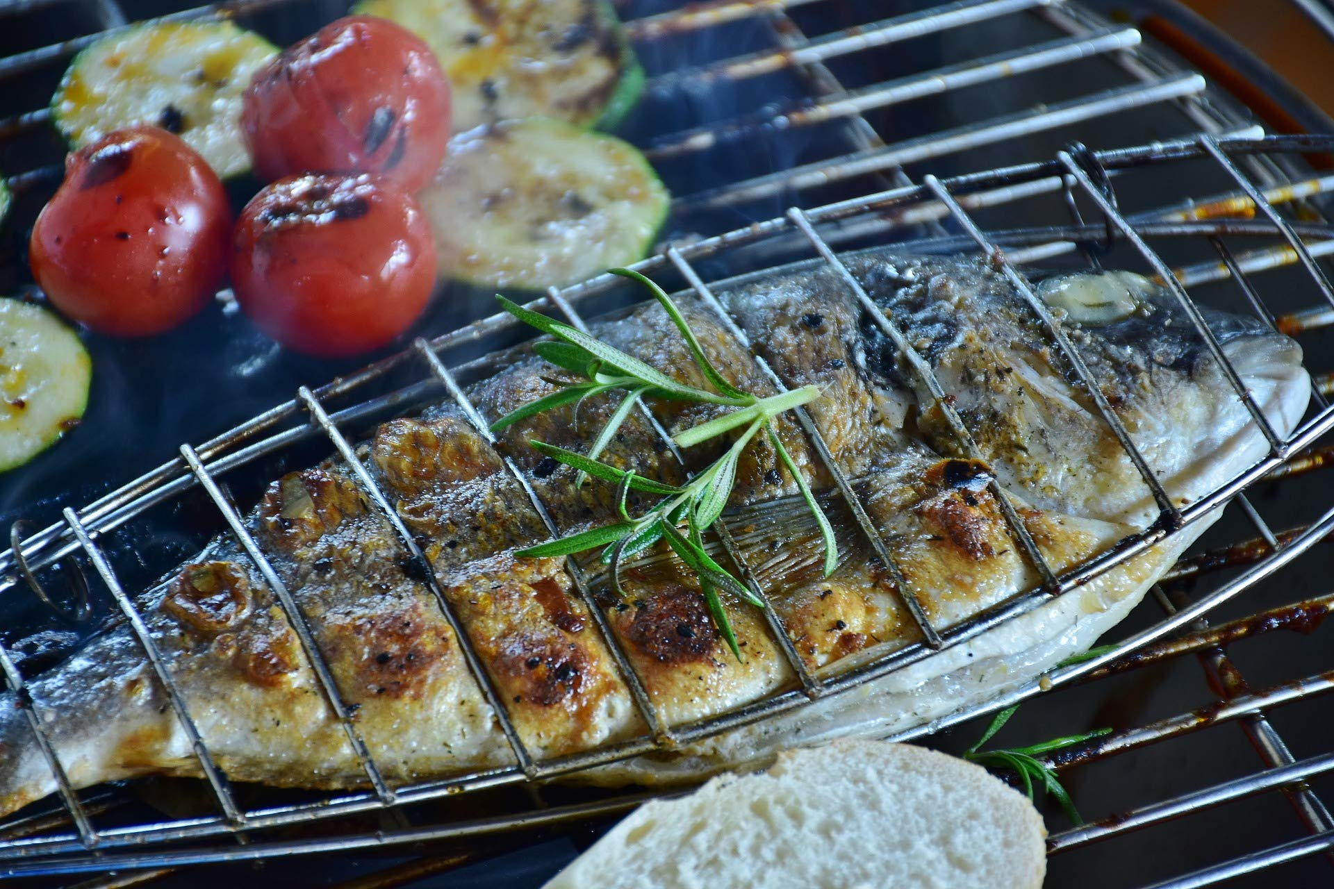 Pesce grigliato con rosmarino, pomodori e fette di zucchine su una griglia.
