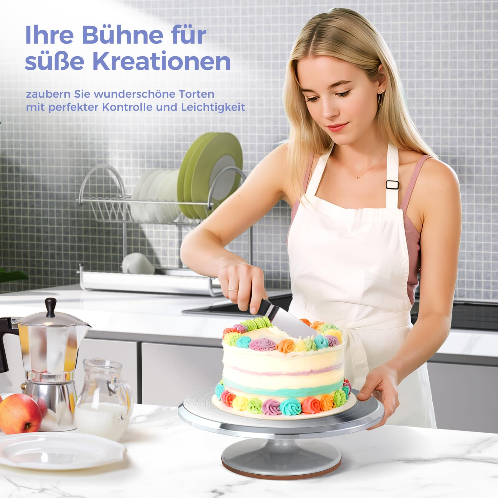 Eine Frau in weißer Schürze verziert eine bunte Torte auf einem Drehteller in einer Küche.