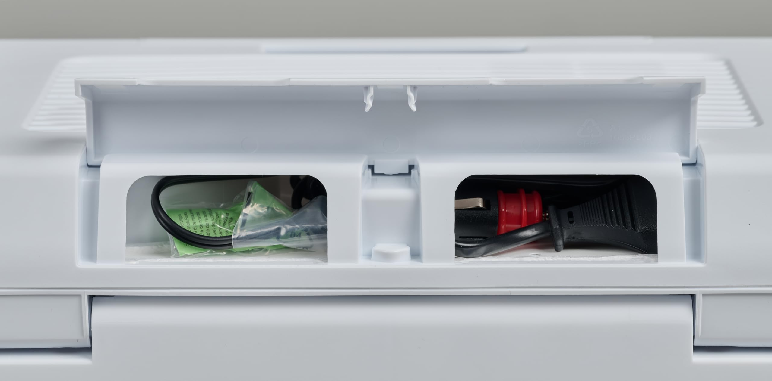 Un compartiment en plastique blanc avec couvercle ouvert, révélant des câbles noirs et un adaptateur allume-cigare rouge.