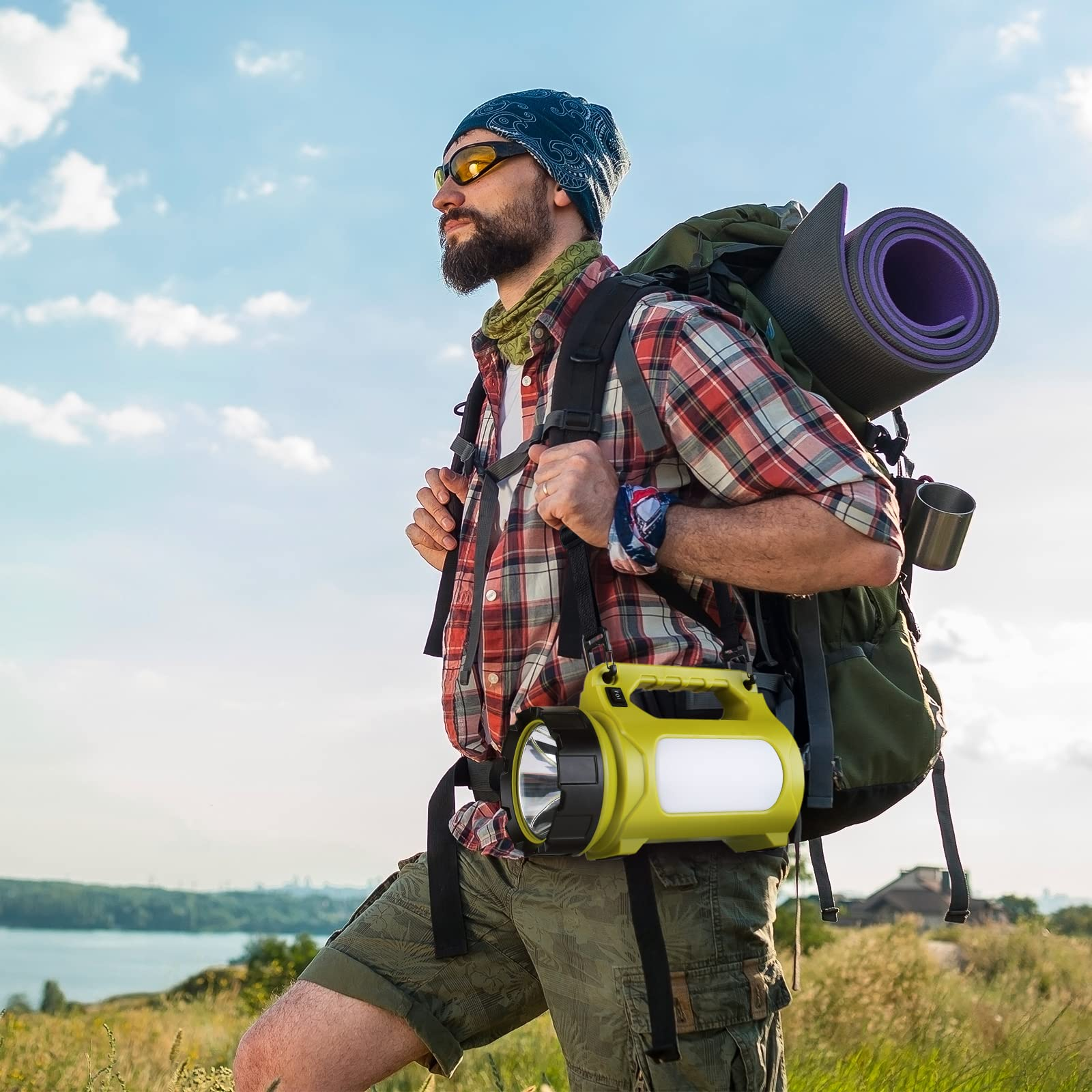 Un randonneur barbu avec un sac à dos et une lanterne jaune, dehors sous un ciel bleu.