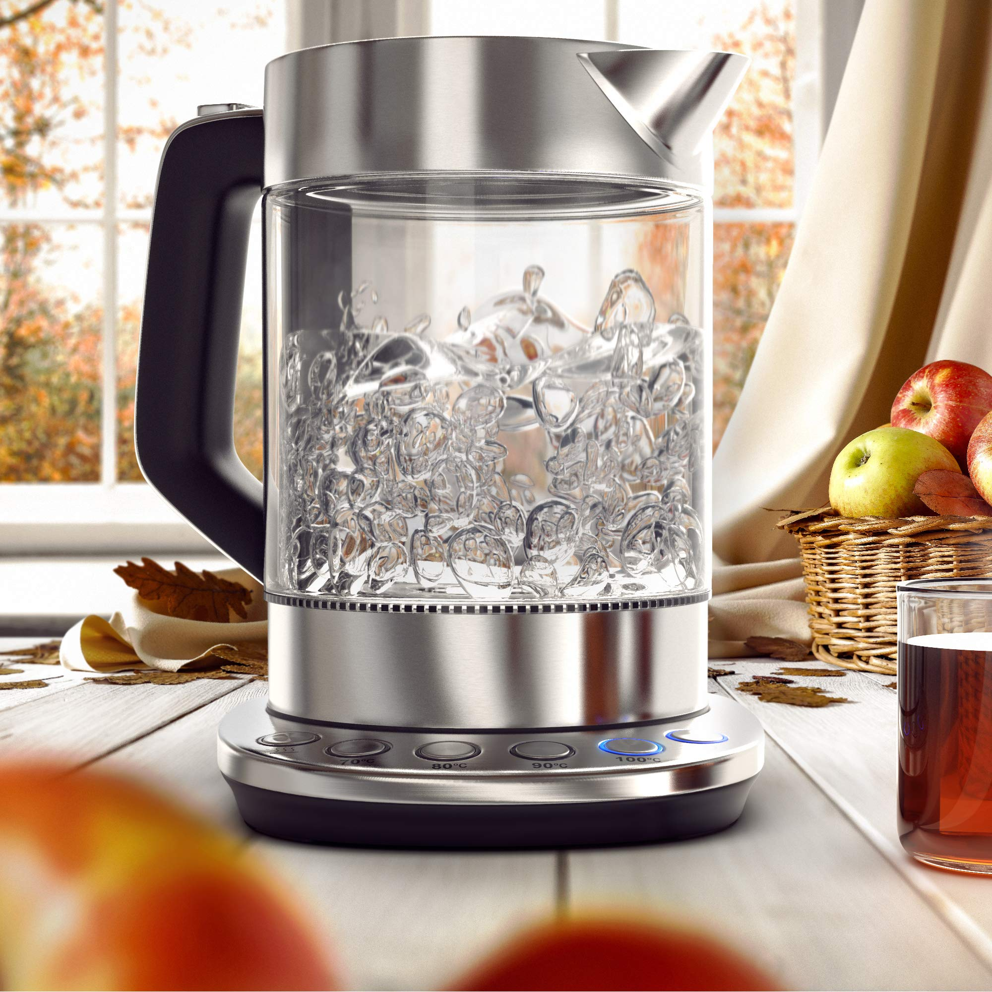 Glaswasserkocher mit kochendem Wasser auf einem Holztisch, im Hintergrund herbstliches Fenster.