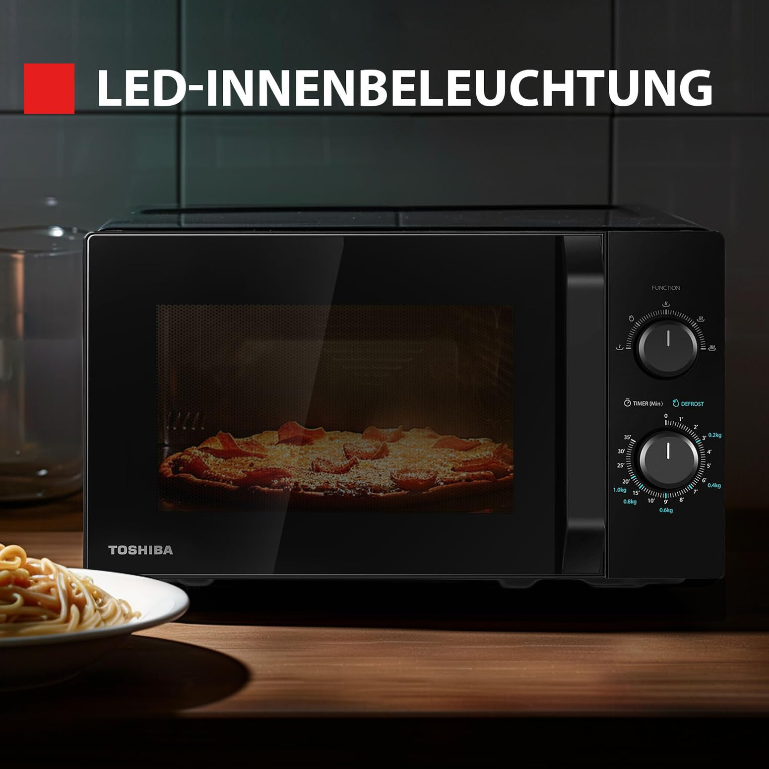 Eine schwarze Toshiba Mikrowelle auf einer Holzarbeitsplatte mit Pizza innen und Pasta davor.